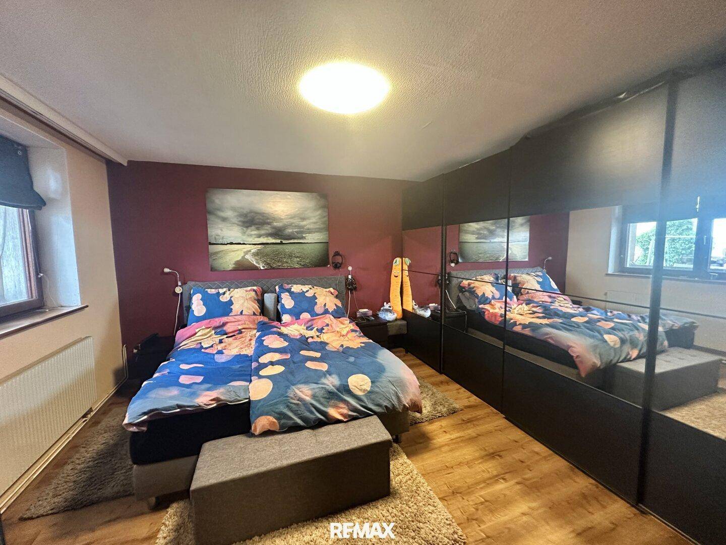 Schlafzimmer mit Doppelbett, großem Spiegelschrank und Holzboden.