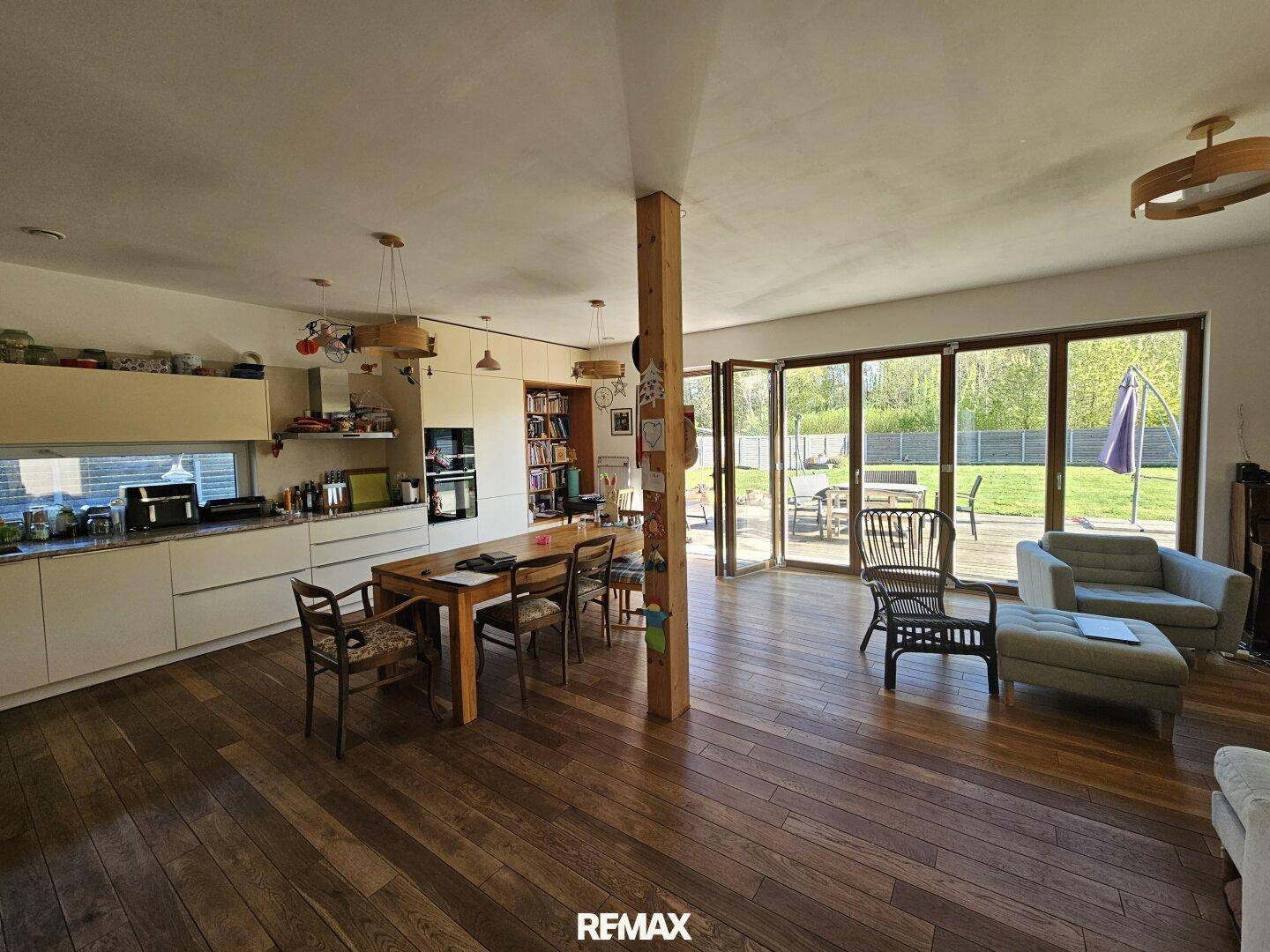 Offener Wohn-Essbereich mit moderner Küche, Holzboden und großzügigem Zugang zur Terrasse.
