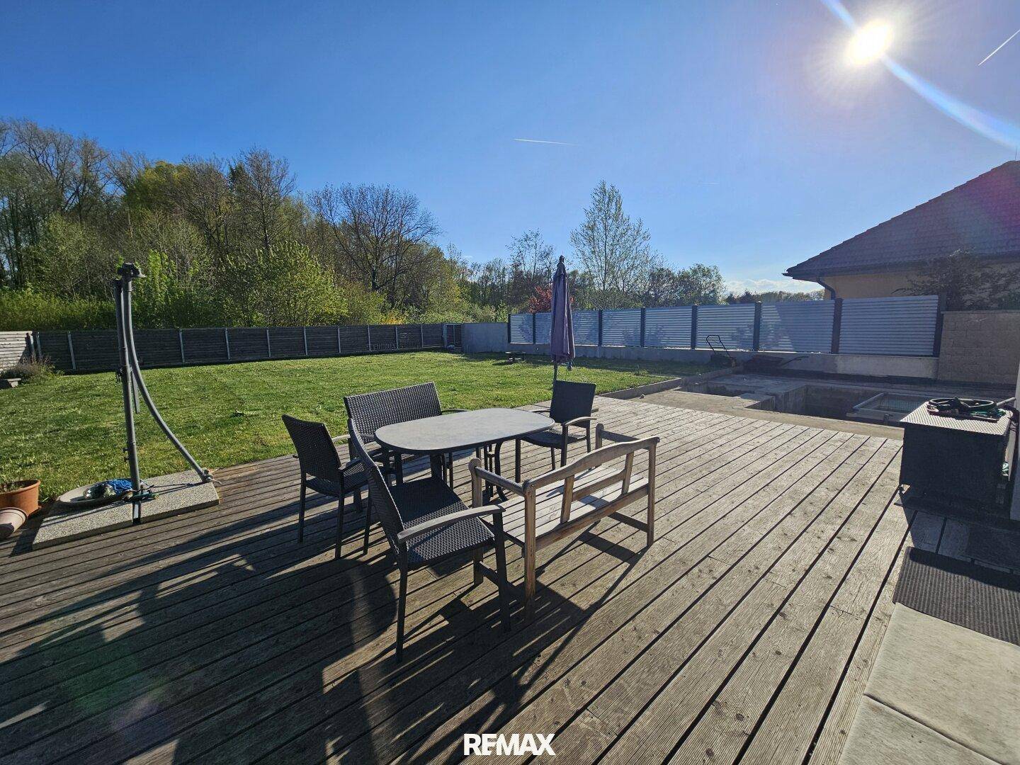 Sonnige Holzterrasse mit Gartenmöbeln und Blick auf den weitläufigen Rasenbereich.