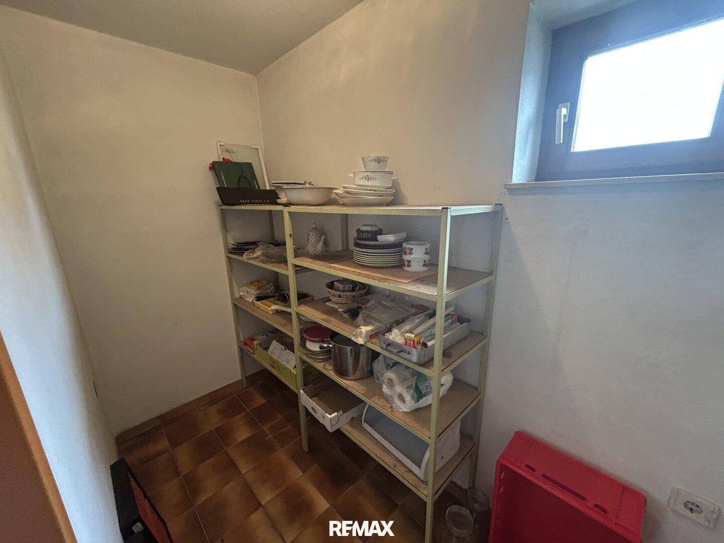 Praktische Speisekammer mit Regalen für Geschirr und Vorräte, gut beleuchtet durch ein Fenster.