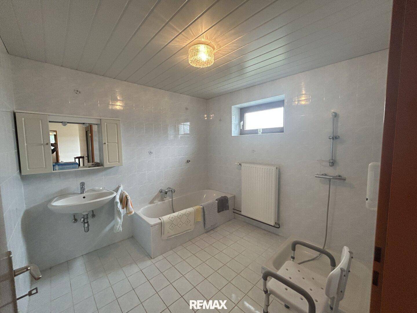 Geräumiges Badezimmer mit weißen Fliesen, Badewanne, Waschbecken und Fenster.