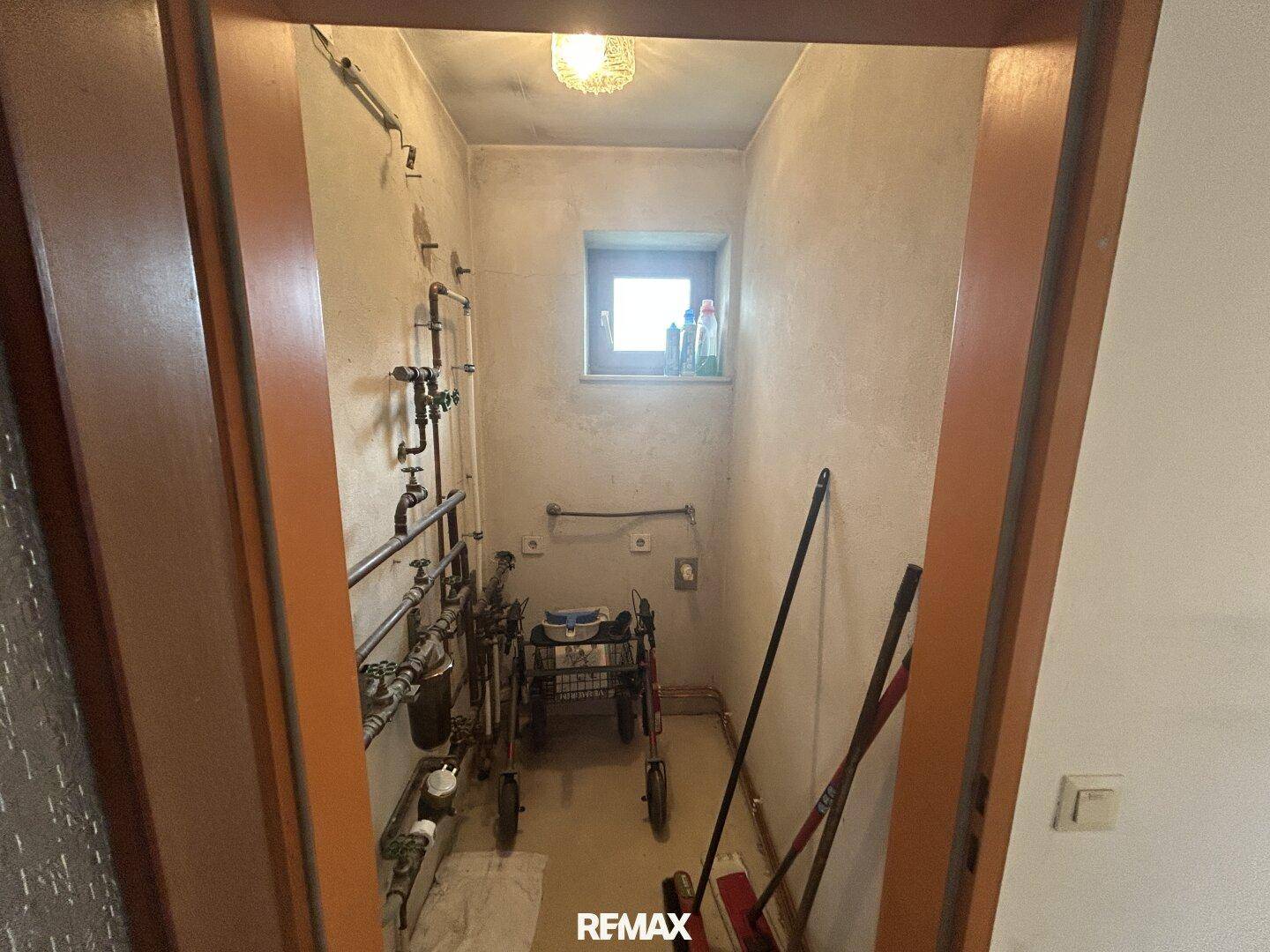 Kleiner Abstellraum mit sichtbaren Rohren und einem Fenster, ideal für Lagerzwecke.