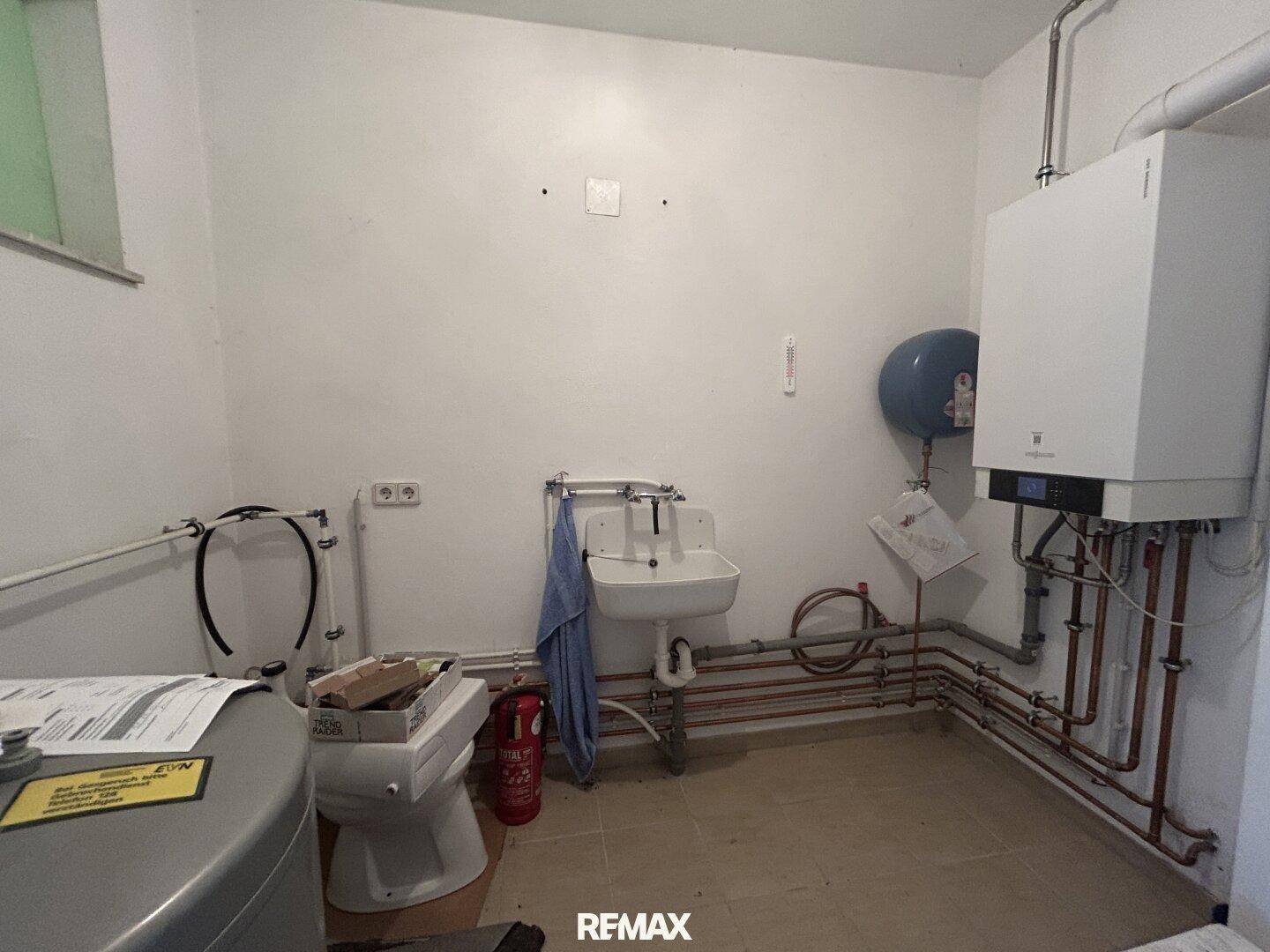 Technikraum mit Heizungsanlage, Warmwasserspeicher und Waschbecken, funktional eingerichtet.