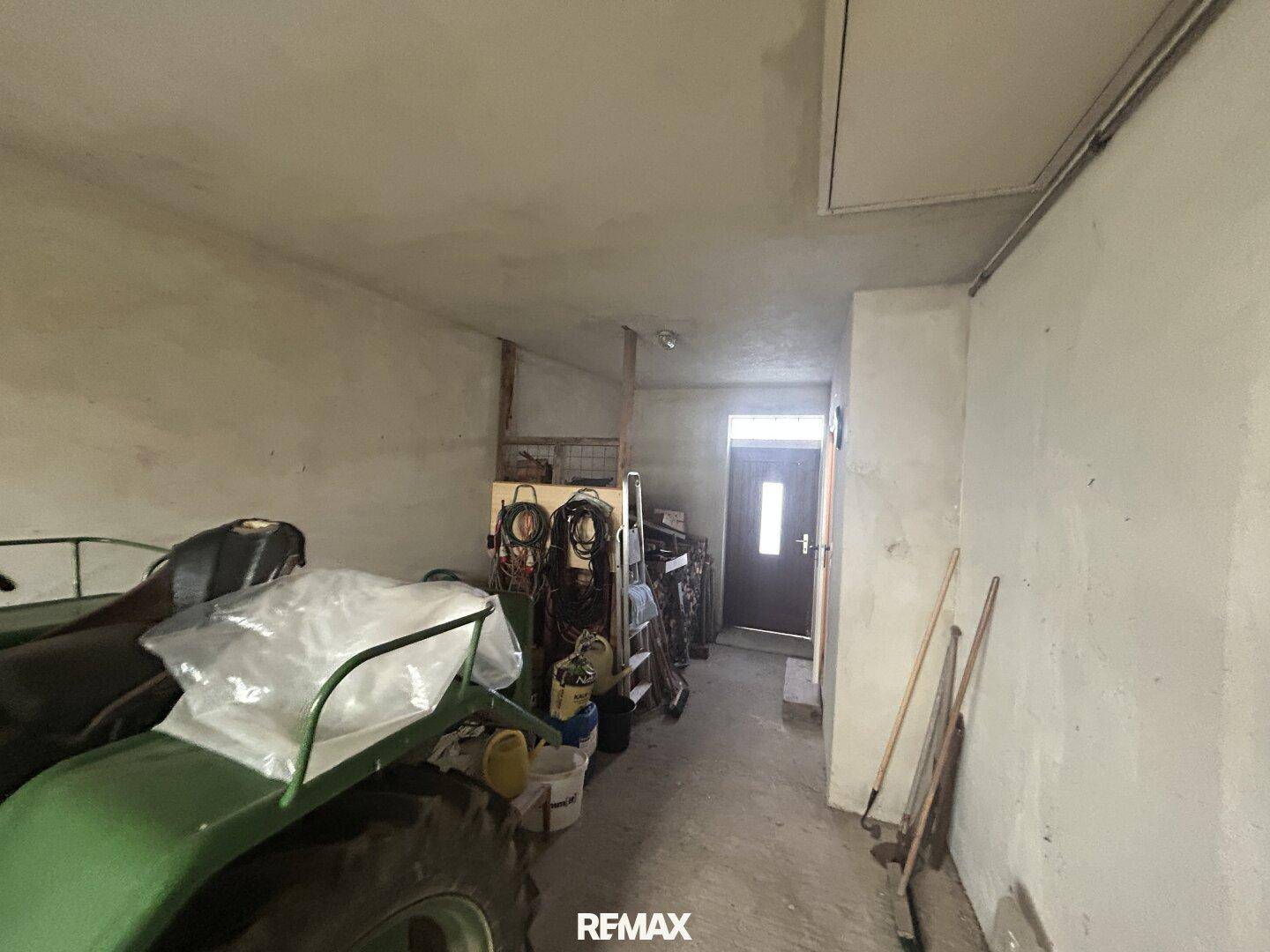 Geräumige Garage mit Betonboden, Platz für Fahrzeuge und Werkzeuge, mit Zugangstür.
