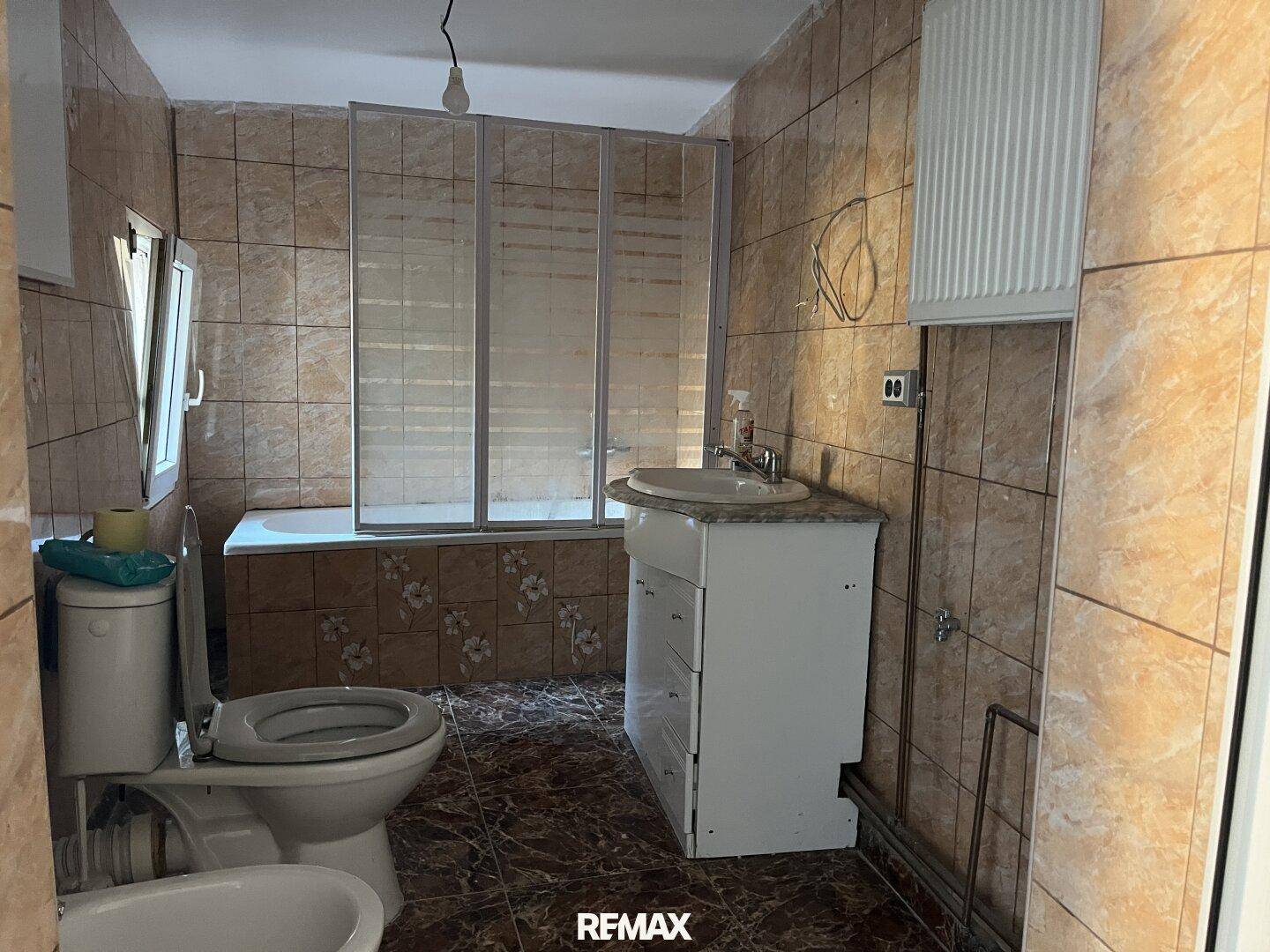 Badezimmer mit braunen Fliesen, Badewanne mit Duschabtrennung, Toilette und Bidet.