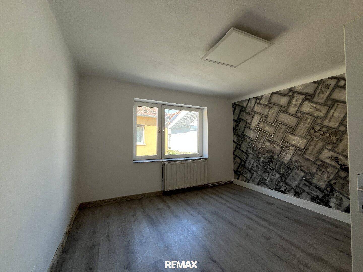 Schlafzimmer mit modernem Laminatboden und einer Akzentwand in Steinoptik.