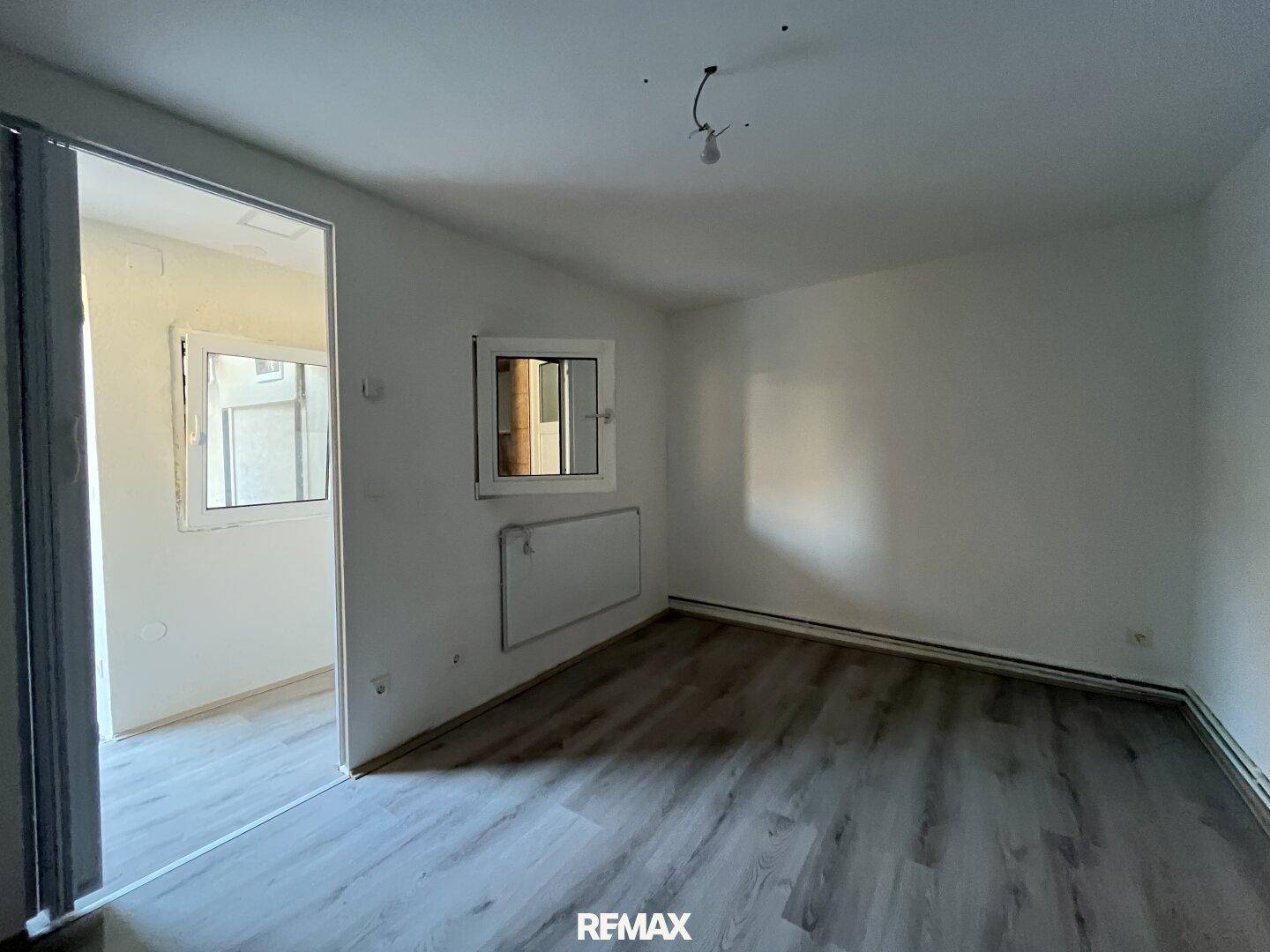 Heller Raum mit Laminatboden und Zugang zu einem weiteren Zimmer durch eine Schiebetür.