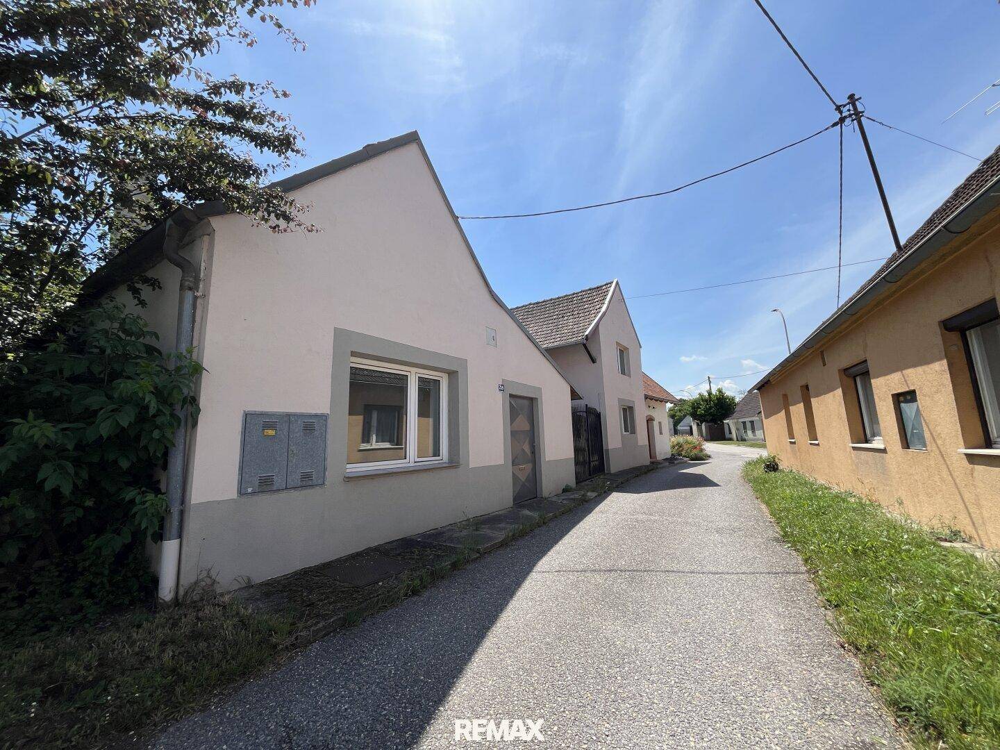 Ländliche Straße mit Wohnhäusern unter blauem Himmel, umgeben von Grünflächen.