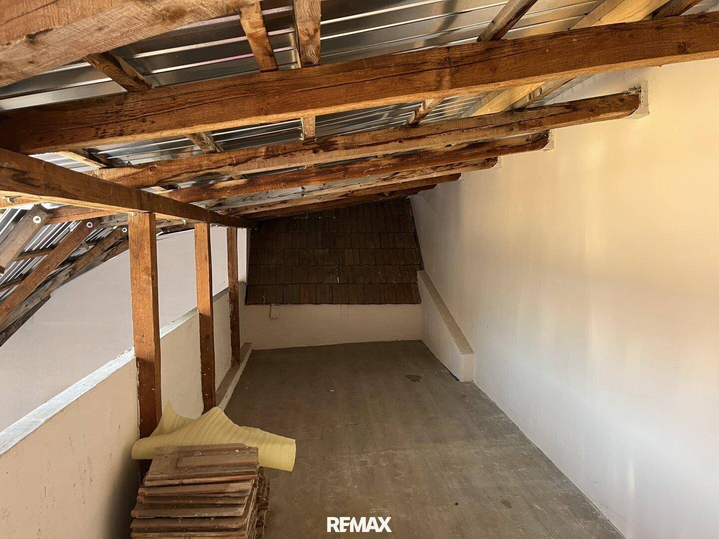 Unausgebauter Dachbodenbereich mit sichtbaren Holzbalken und Lagerfläche.