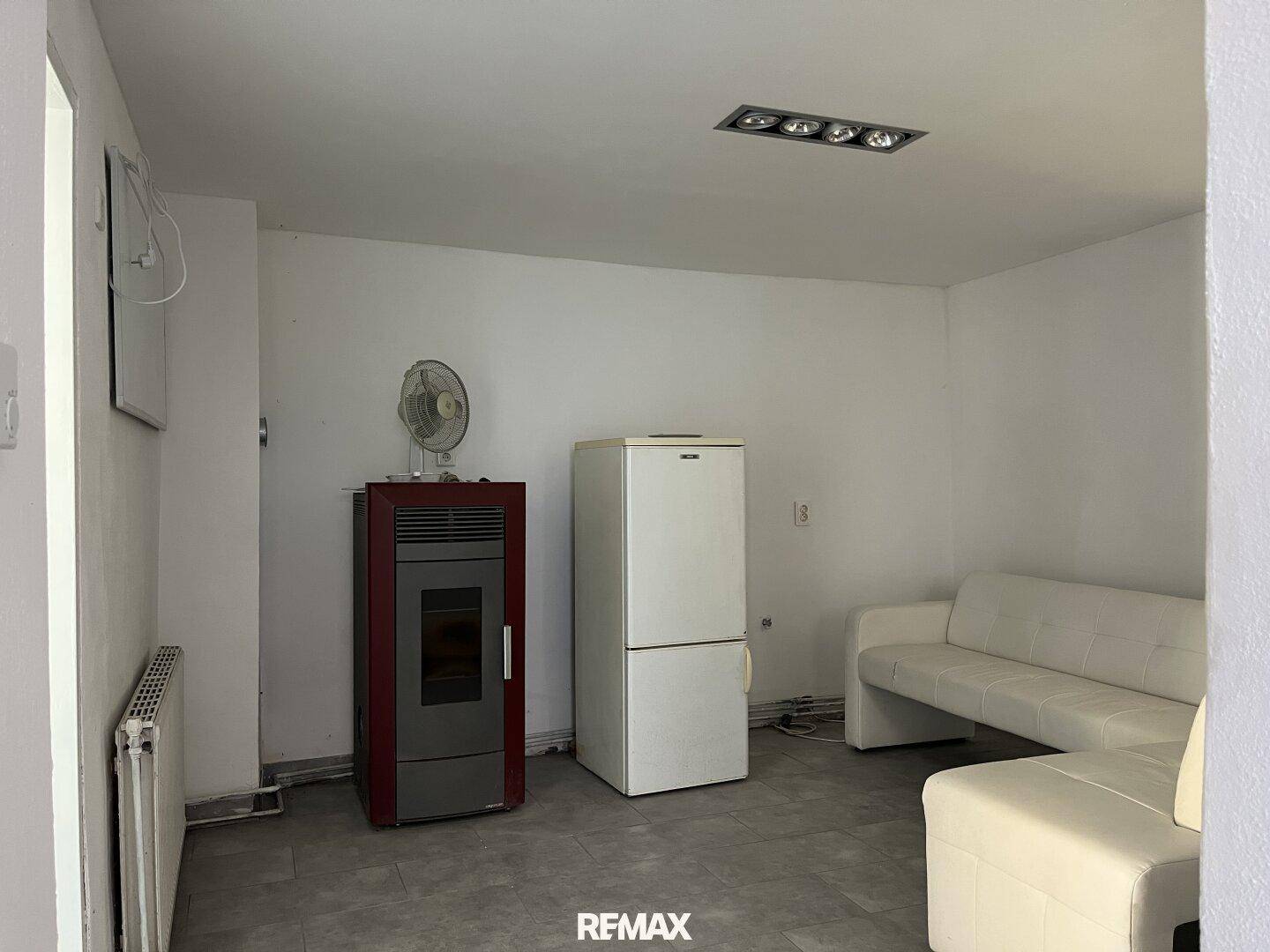 Wohnbereich mit Pelletofen, Kühlschrank und einer hellen Couch, ideal für gemütliche Abende.