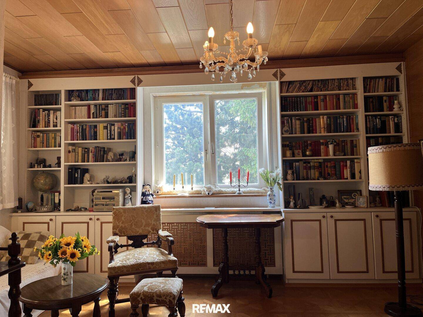 Wohnzimmer mit großen Bücherregalen, Holzbalkendecke und Kronleuchter, hell und einladend.