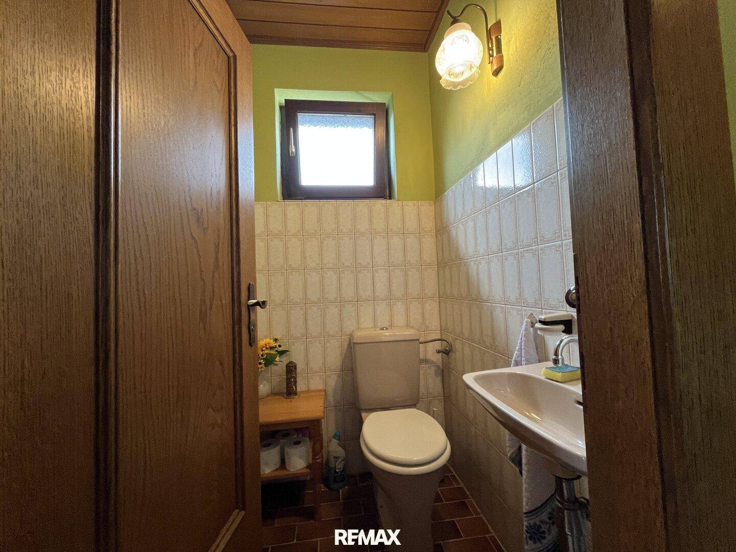 Kleines Gäste-WC mit Fliesen, Fenster und einfacher Ausstattung in hellgrünen Farbtönen.