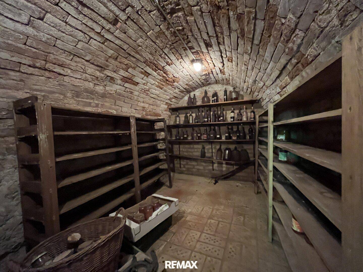 Rustikaler Kellerraum mit Ziegelwänden, gewölbter Decke und Holzregalen für Lagerung.
