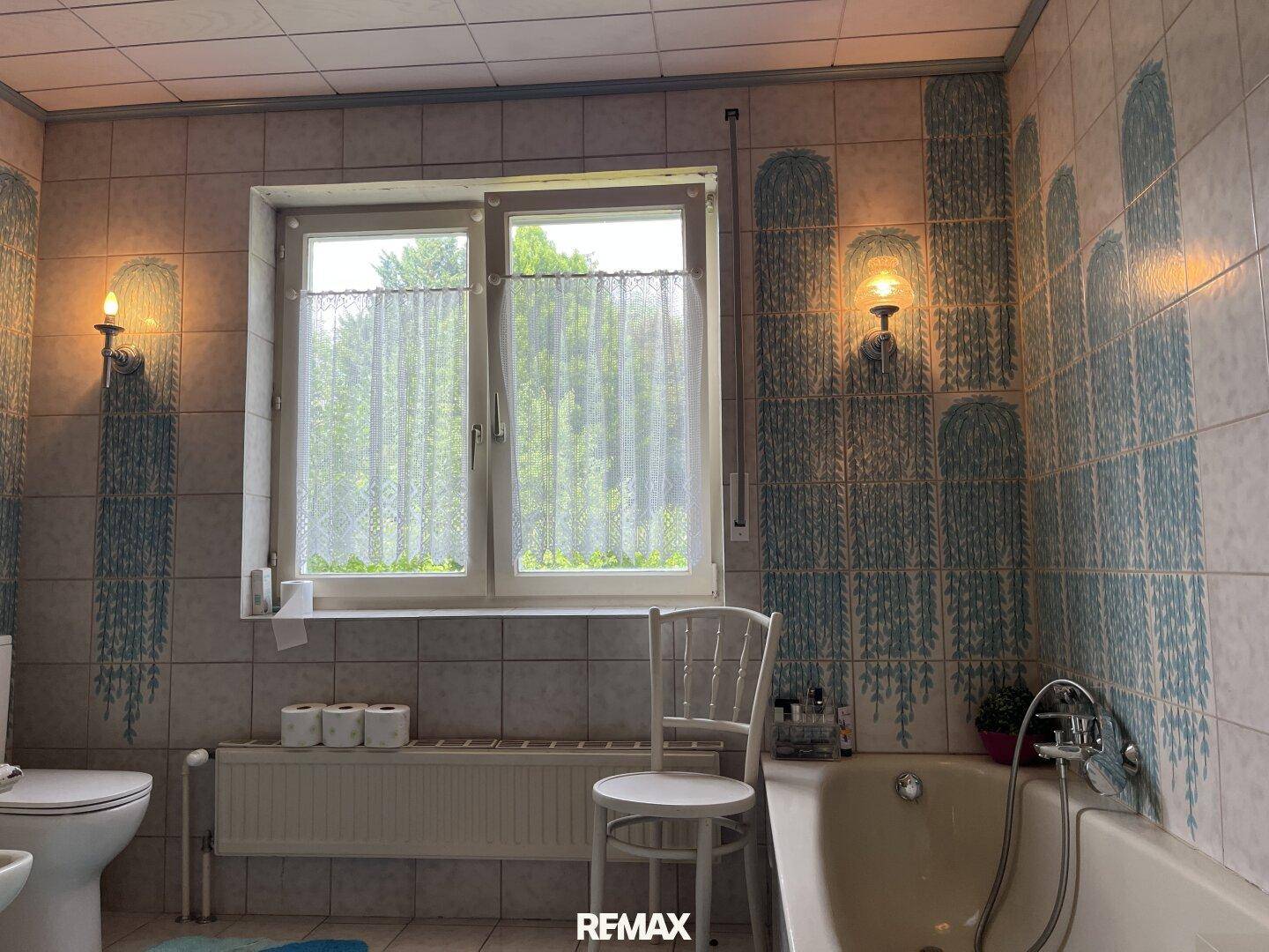 Badezimmer mit Badewanne, WC und Fenster, dekoriert mit blauen Fliesen im 80er-Jahre-Stil.