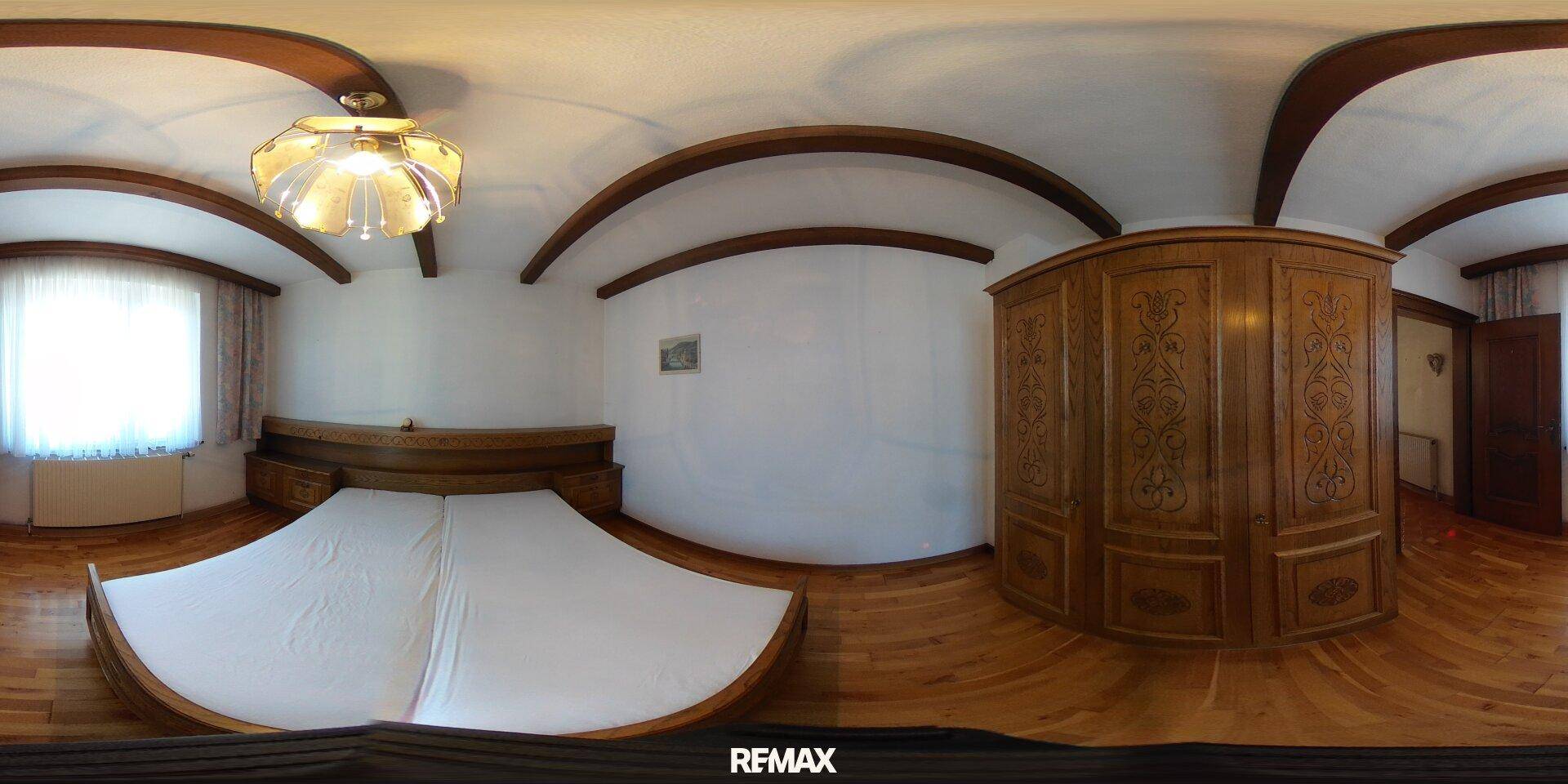 Schlafzimmer mit einem runden Holzbett, geschnitztem Kleiderschrank und Parkettboden.