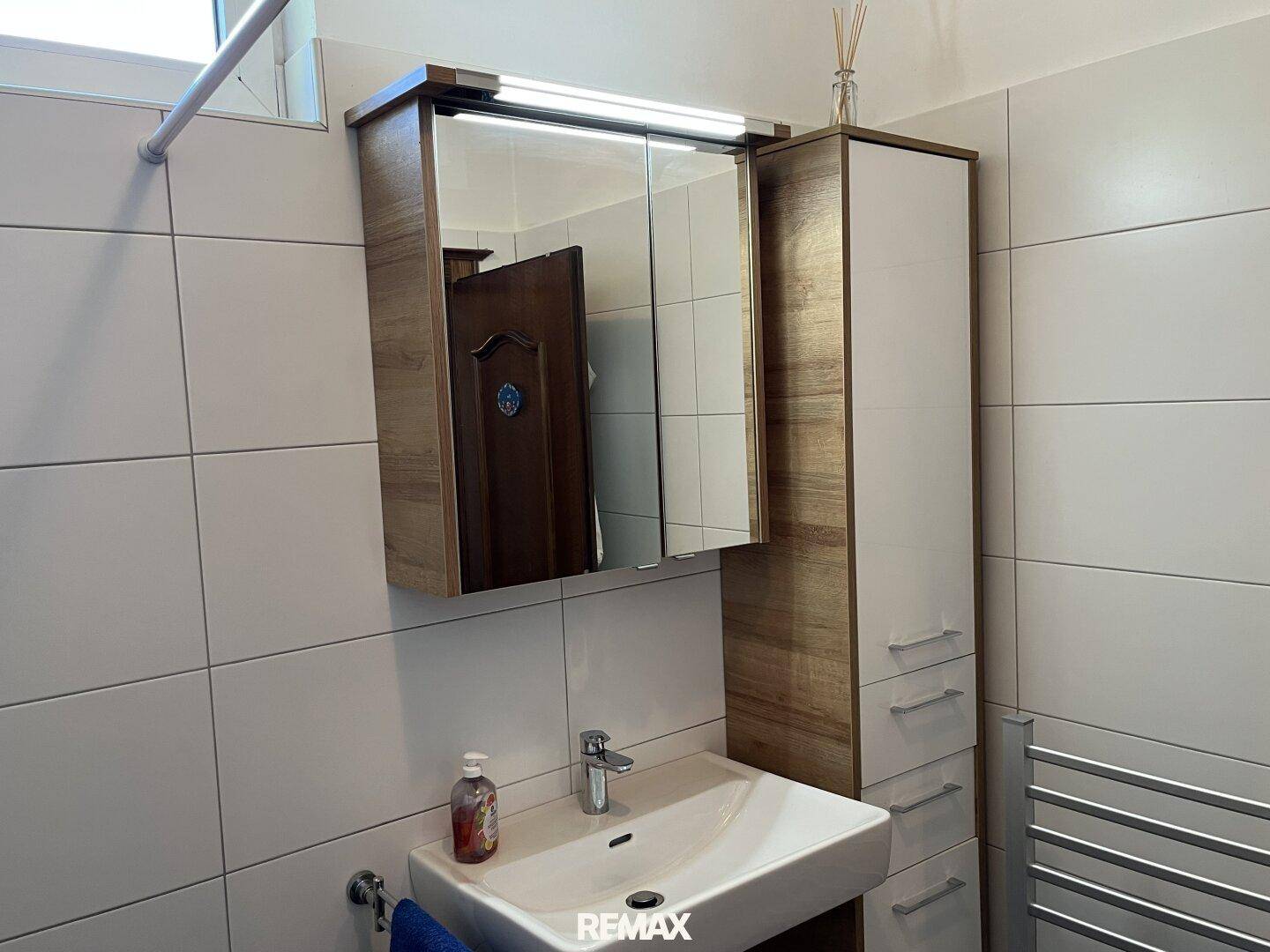 Modernisiertes Badezimmer mit hellem Fliesenboden, Einzelwaschbecken und Spiegelschrank.