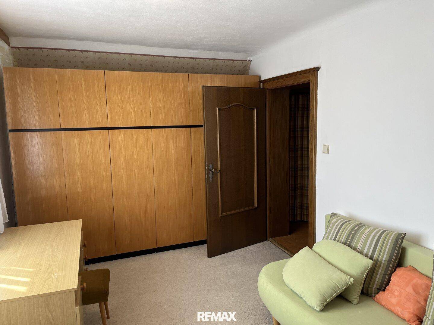 Zimmer mit großem Holzschrank, Sofa und Teppichboden, nutzbar als Schlaf- oder Gästezimmer.