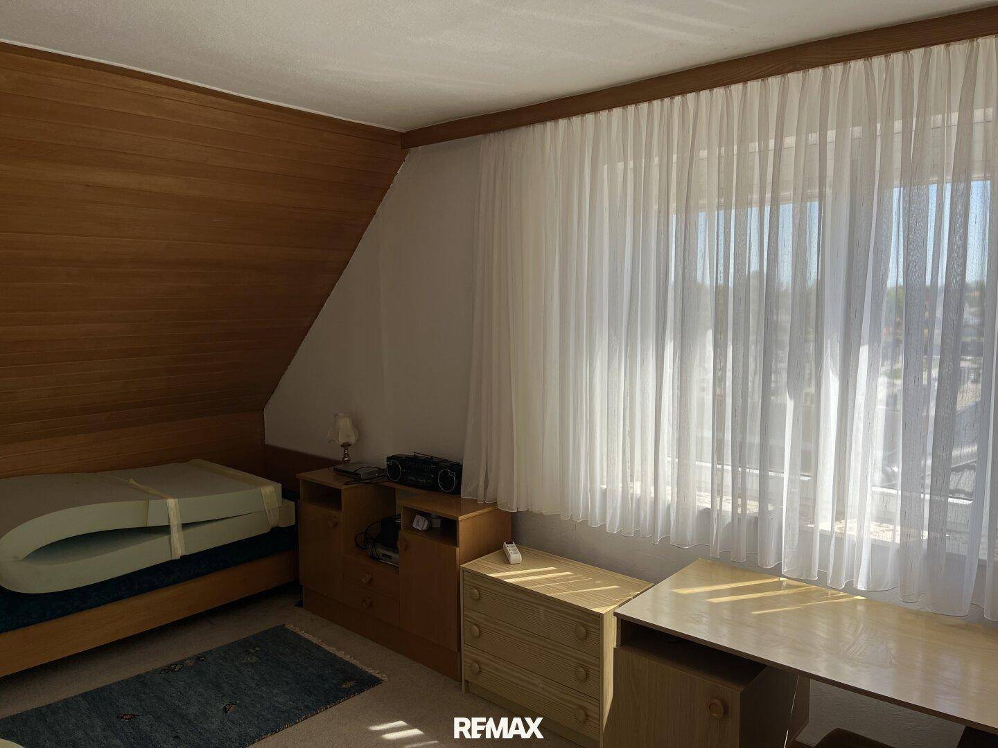 Dachschlafzimmer mit schräger Decke, Holzverkleidung und Fenster für natürliches Licht.