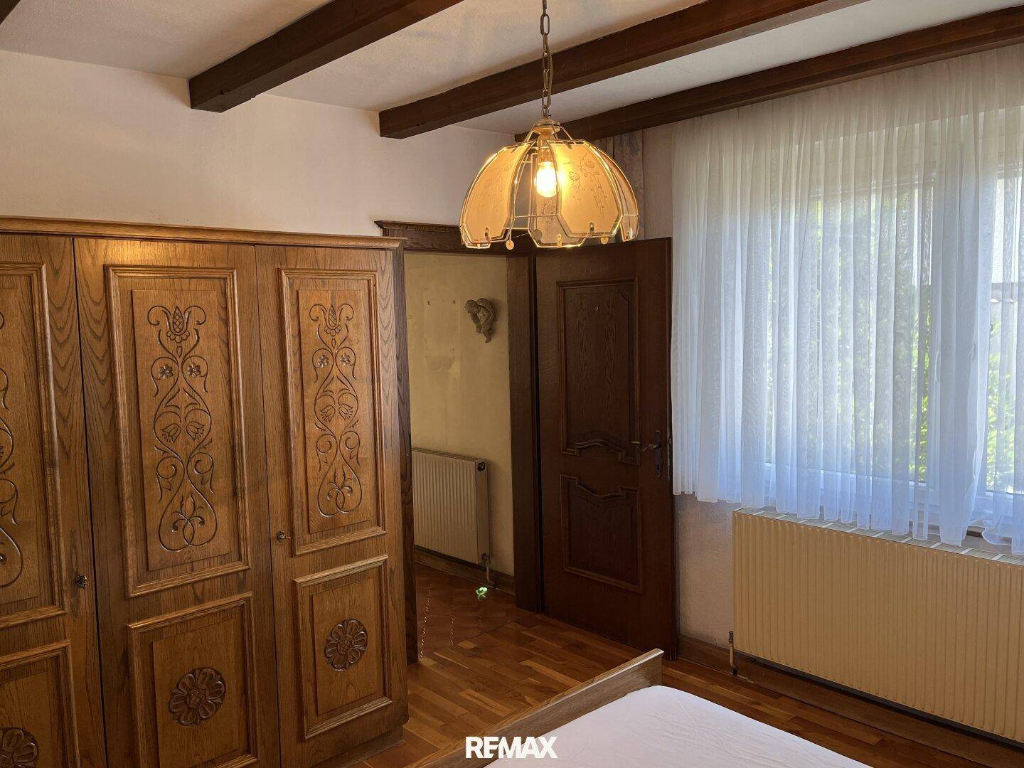 Schlafzimmer mit großem Holzschrank, Holzbalkendecke und Parkettboden, hell durch Fenster.