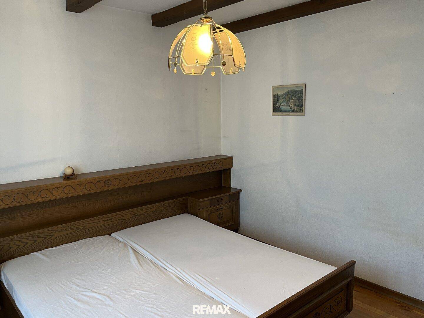 Schlafzimmer mit traditionellem Holzbett, Holzbalkendecke und schlichten weißen Wänden.