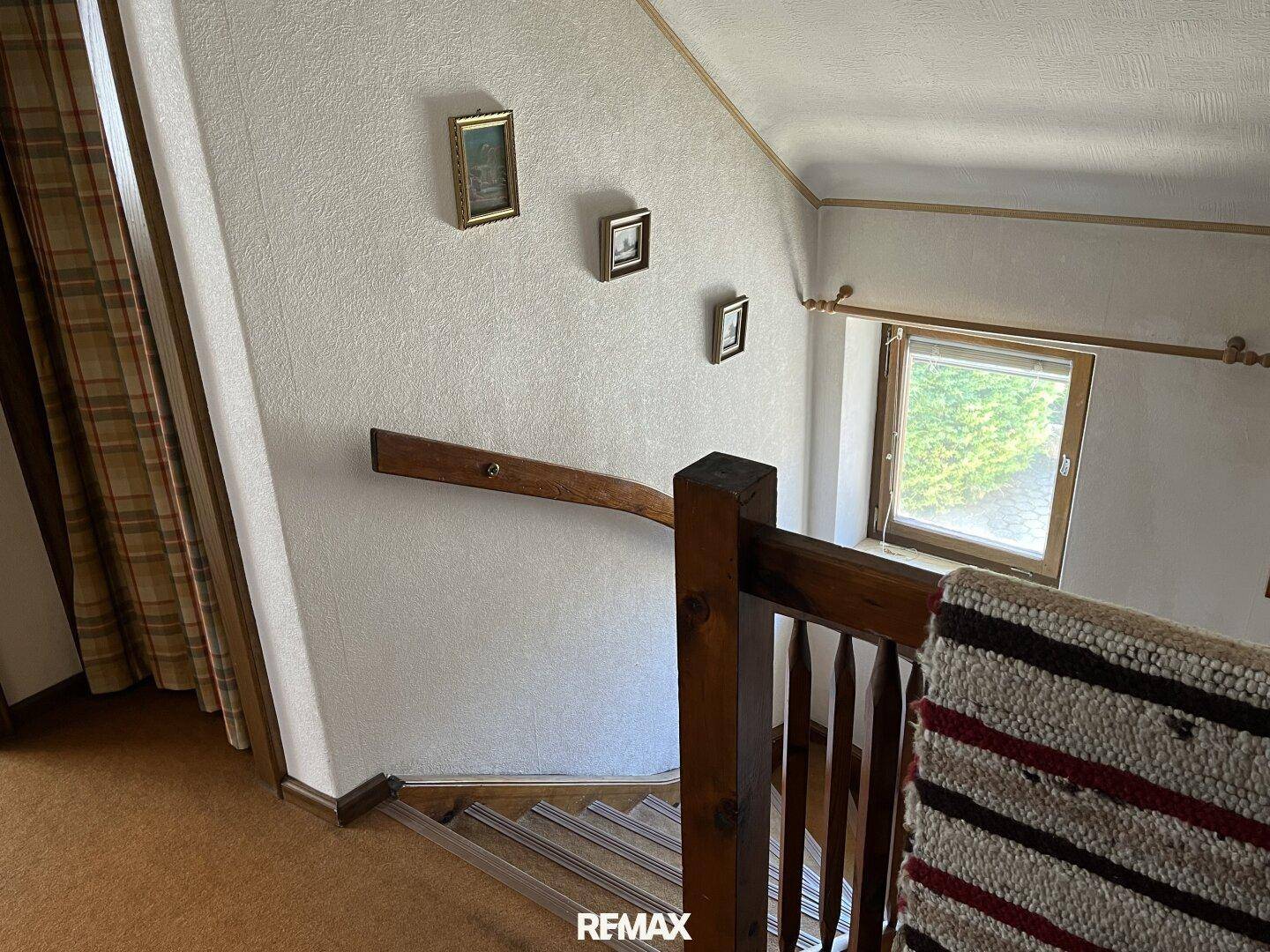 Holztreppe mit Geländer und Fenster, das Tageslicht in den Treppenbereich bringt.