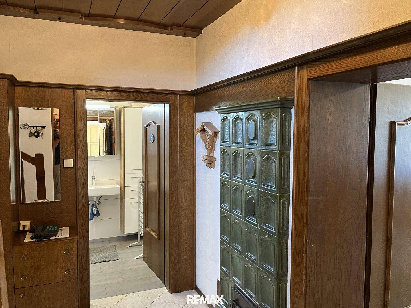 Flur mit grünem Kachelofen und Zugang zu einem modernisierten Badezimmer.