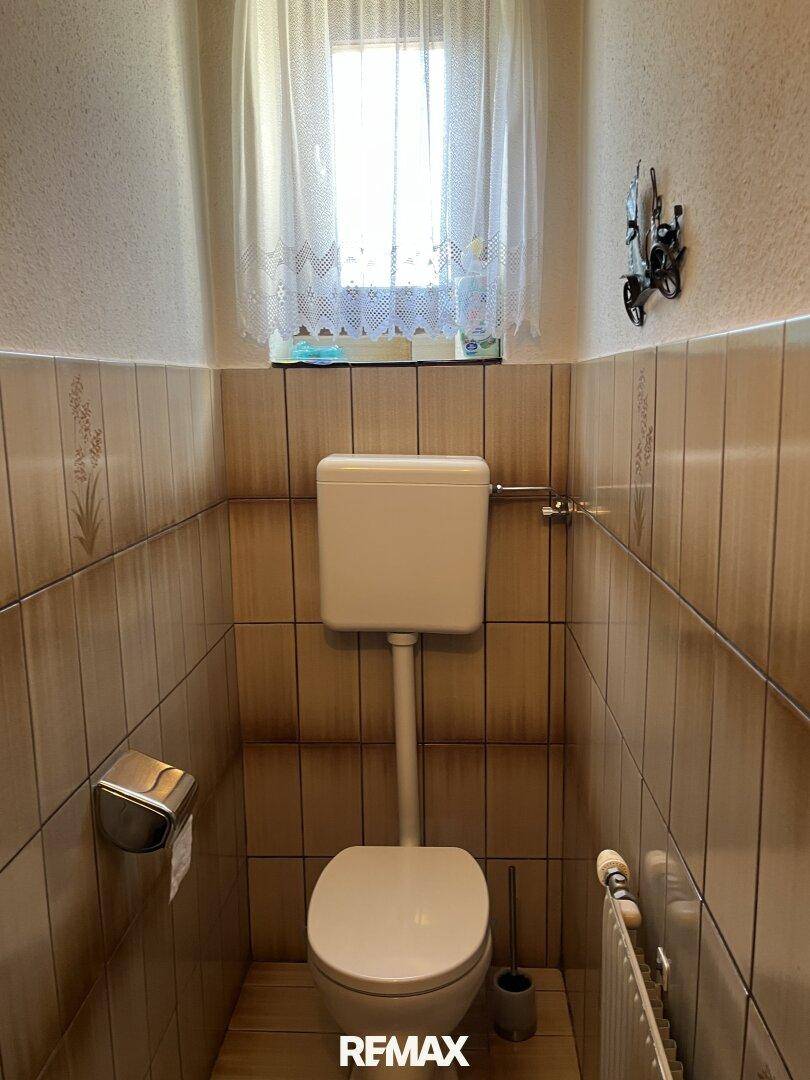 Kleines Gäste-WC mit Fenster, gefliesten Wänden und traditioneller Toilette.