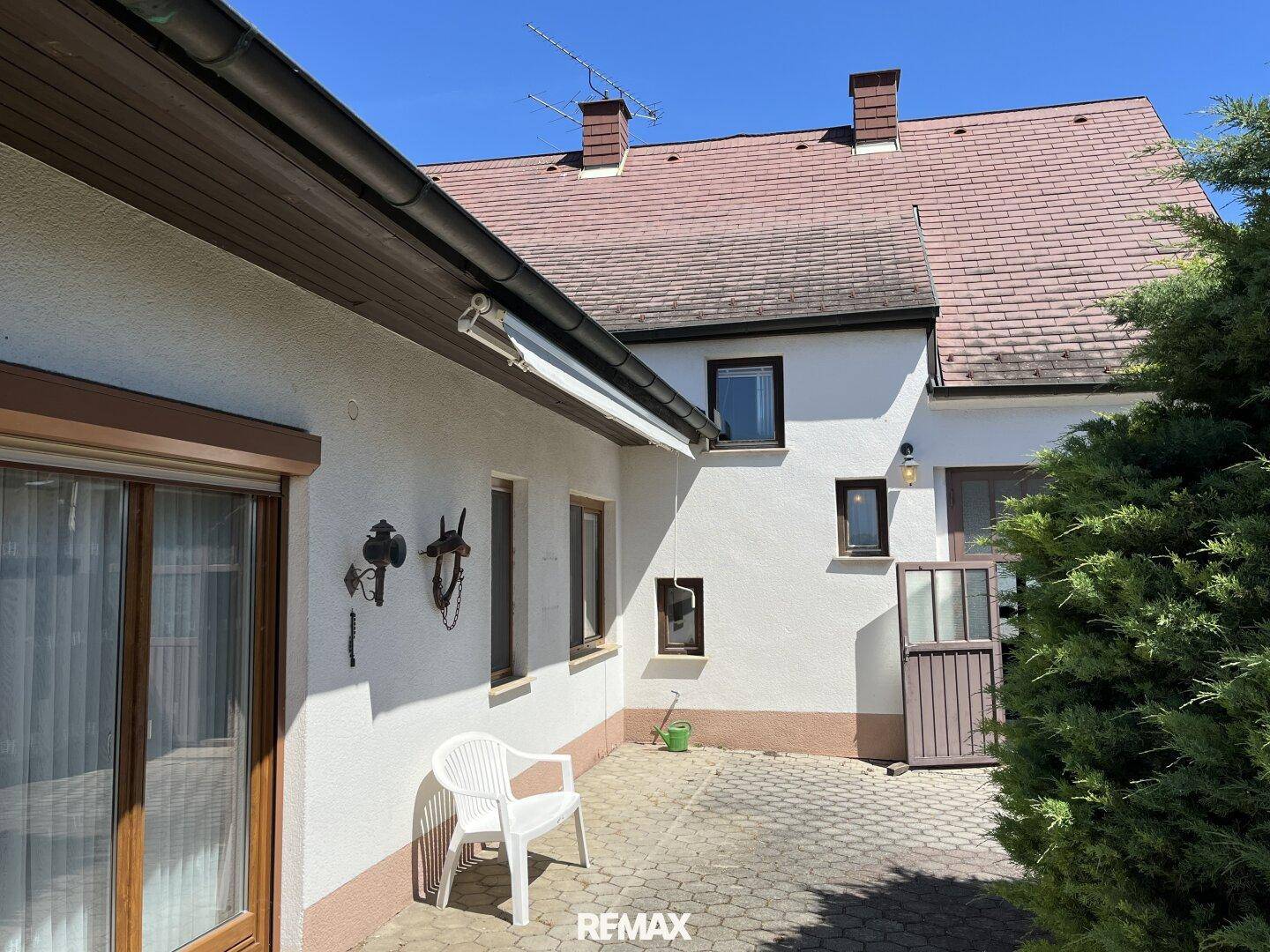 Gepflasterte Terrasse an der Hausseite mit einem einzelnen Stuhl und Blick auf den Garten.