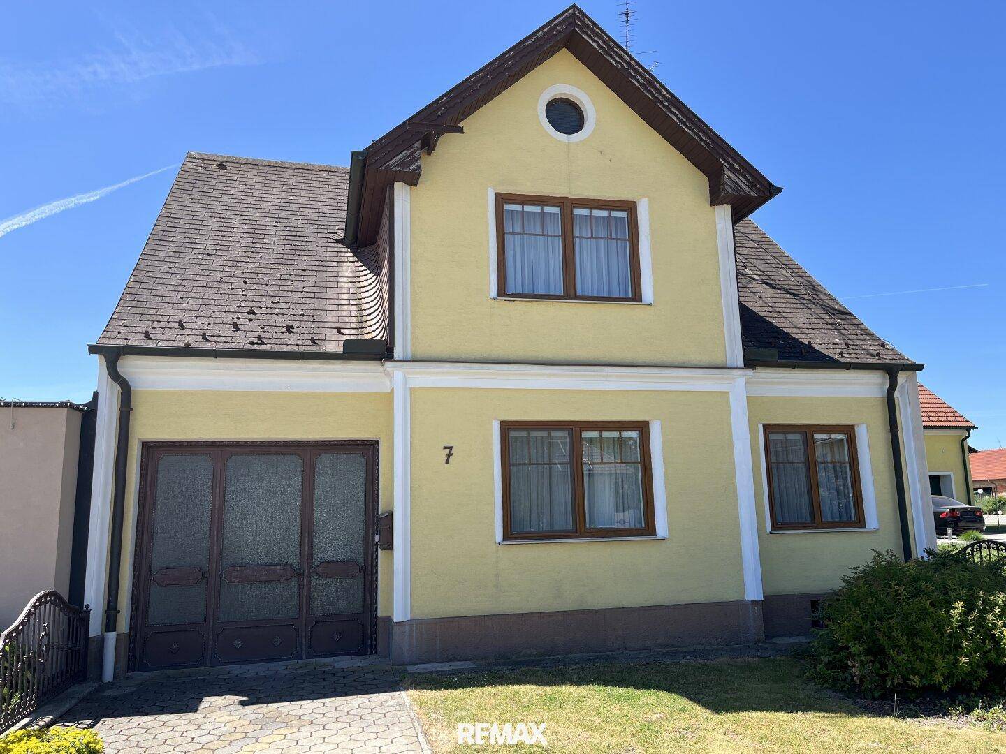 Vorderansicht eines traditionellen gelben Einfamilienhauses mit Satteldach und gepflasterter Einfahrt.
