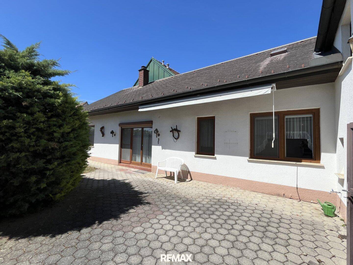 Gepflasterter Außenbereich hinter dem Haus mit einer kleinen Bank und Zugang zum Innenbereich.