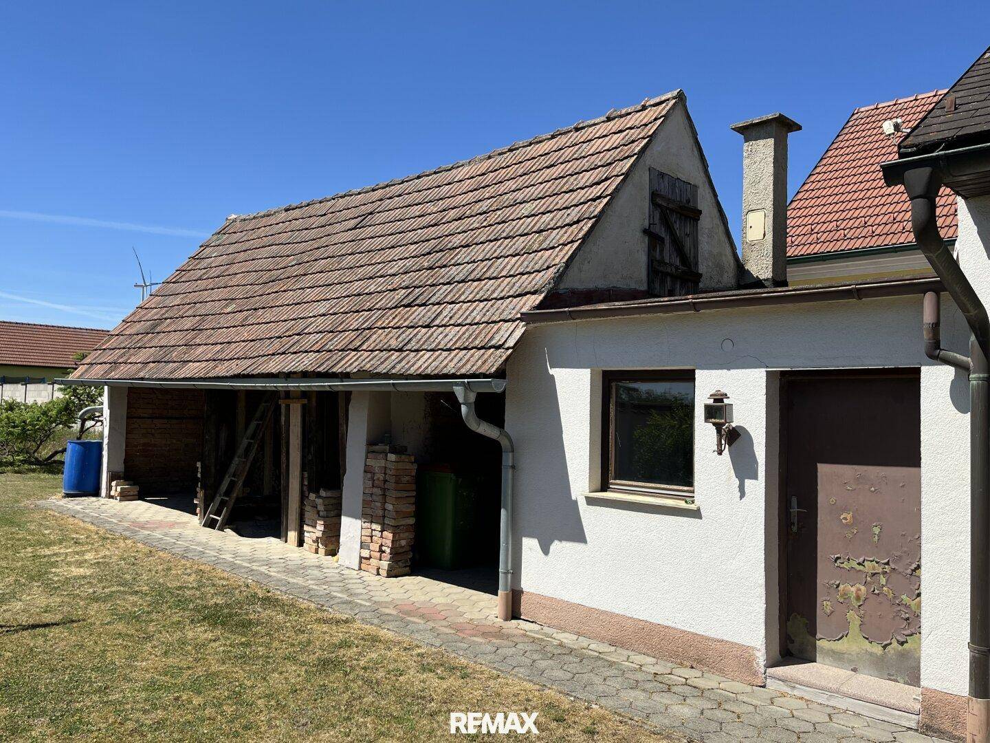 Nebengebäude mit einem Schuppen und gelagertem Holz, umgeben von einer Rasenfläche.