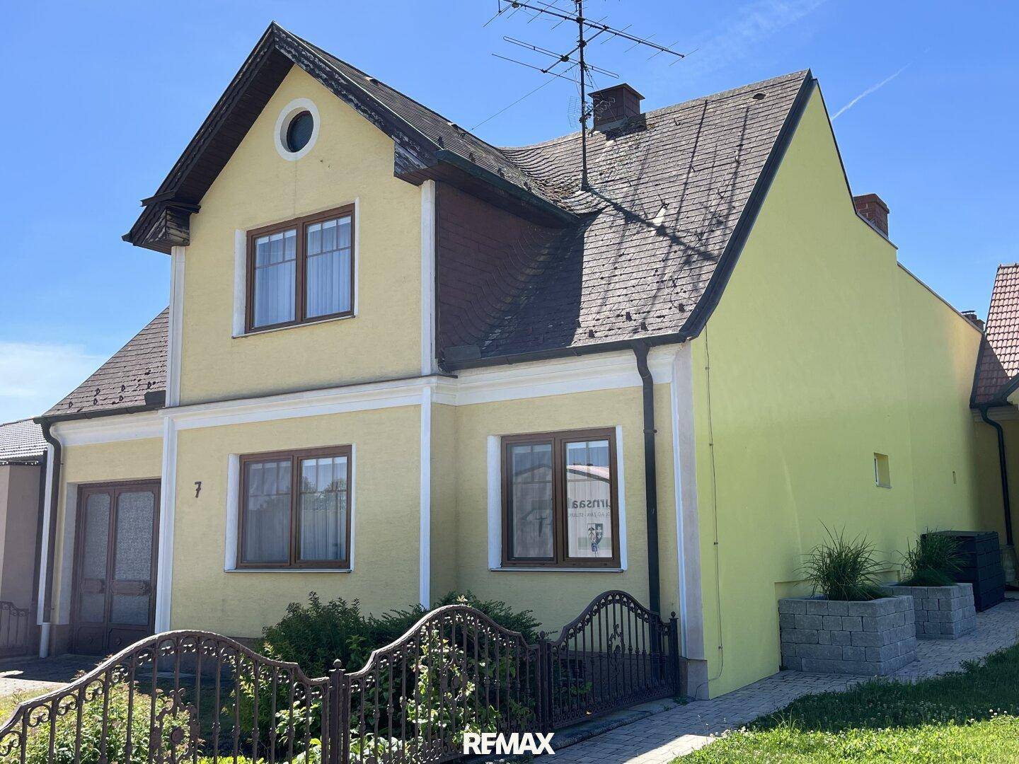 Gelbes Einfamilienhaus mit Satteldach und einem dekorativen Zaun im Vorgarten unter blauem Himmel.