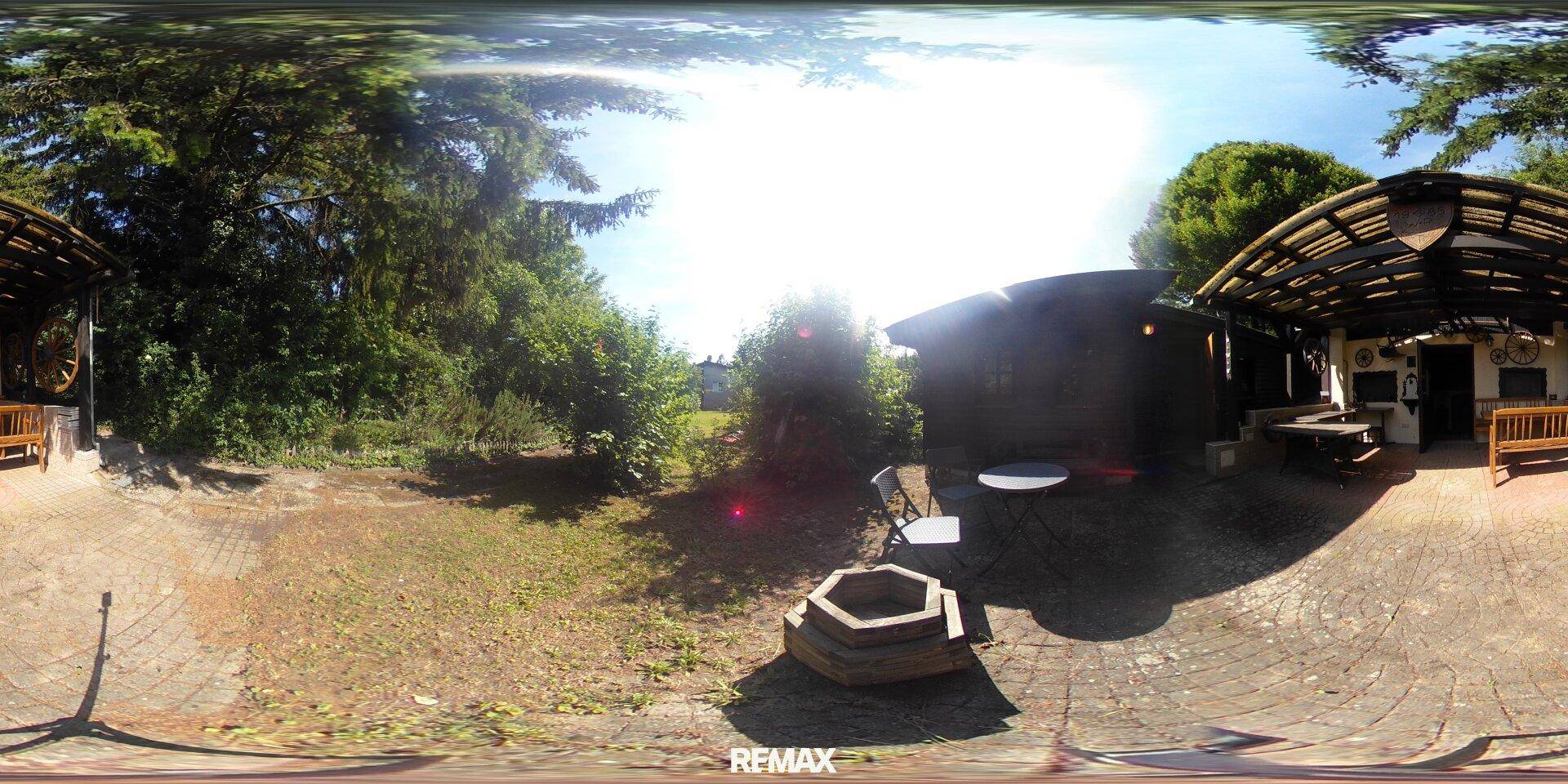 Außenbereich mit gepflasterter Terrasse, Feuerstelle und umgebenden Bäumen.
