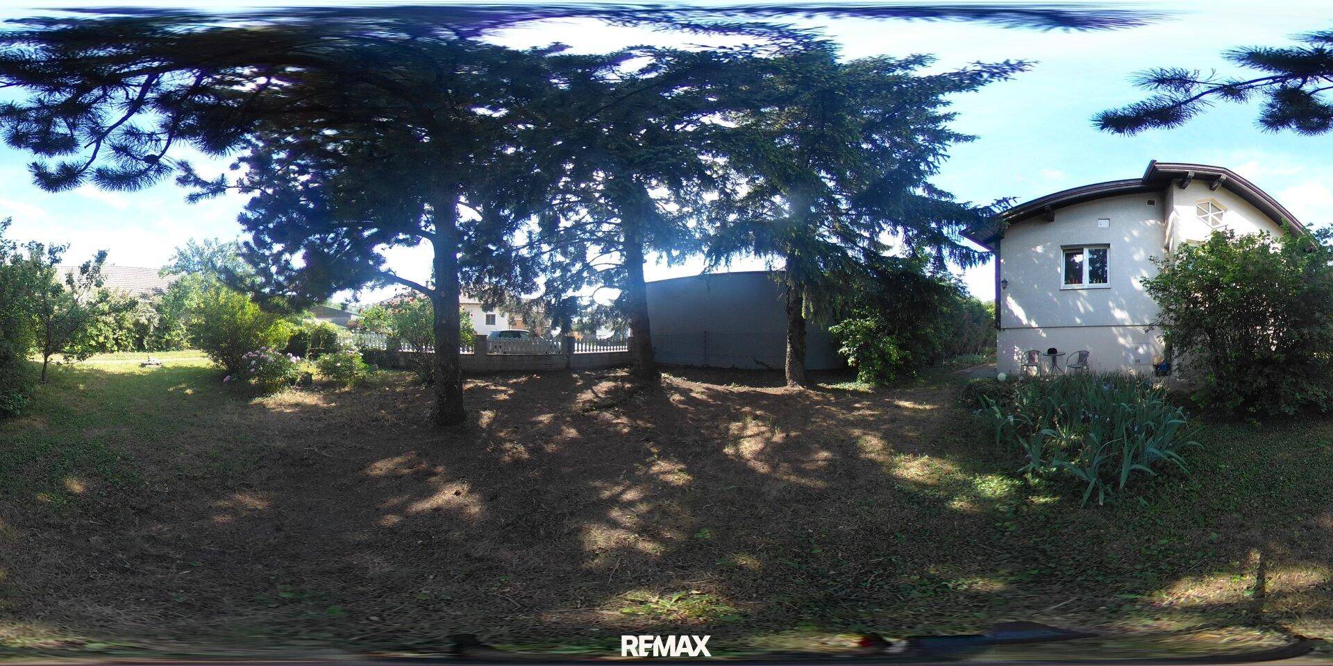 Panoramablick auf das Grundstück mit Haus, Bäumen und weitläufiger Rasenfläche.