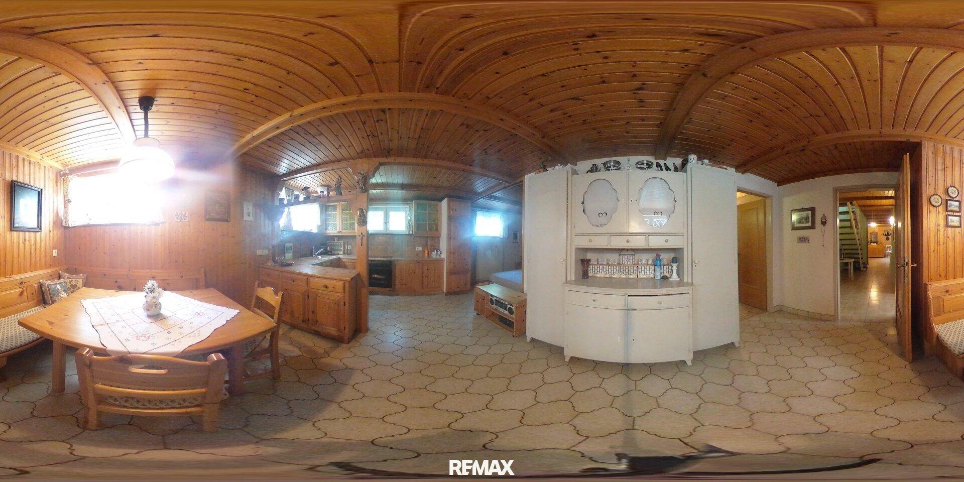 Gemütlicher Essbereich mit Holztisch und Bänken, sowie einer kleinen Küchenzeile im Hintergrund.