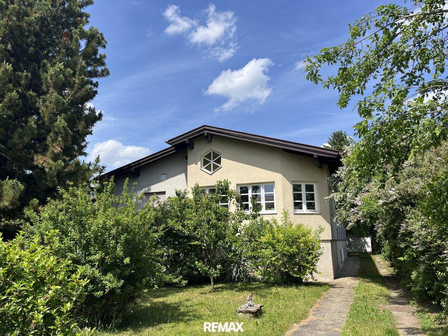 Ansicht des Hauses von außen mit viel Grün und einem gepflasterten Weg unter blauem Himmel.