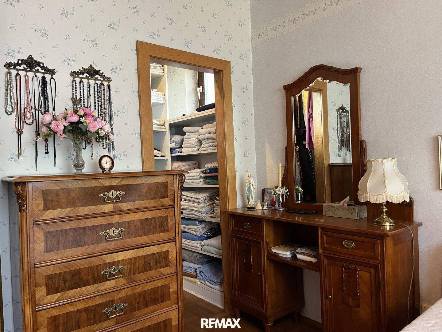 Ankleidebereich im Schlafzimmer mit Holzmöbeln und offenem Zugang zu einem begehbaren Kleiderschrank.