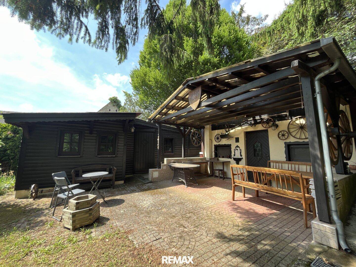 Gemütlicher Außenbereich mit gepflasterter Terrasse, überdachtem Sitzplatz und Gartenhaus.
