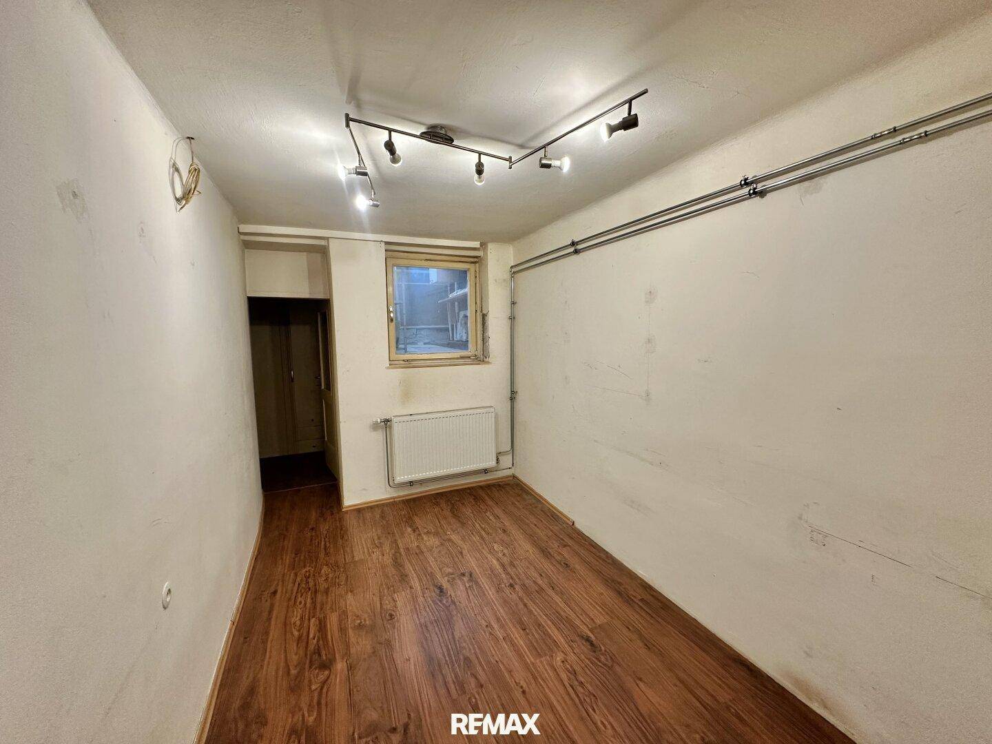 Leerer Raum mit Holzboden, Heizkörper und einem Fenster, bereit zur Neugestaltung.