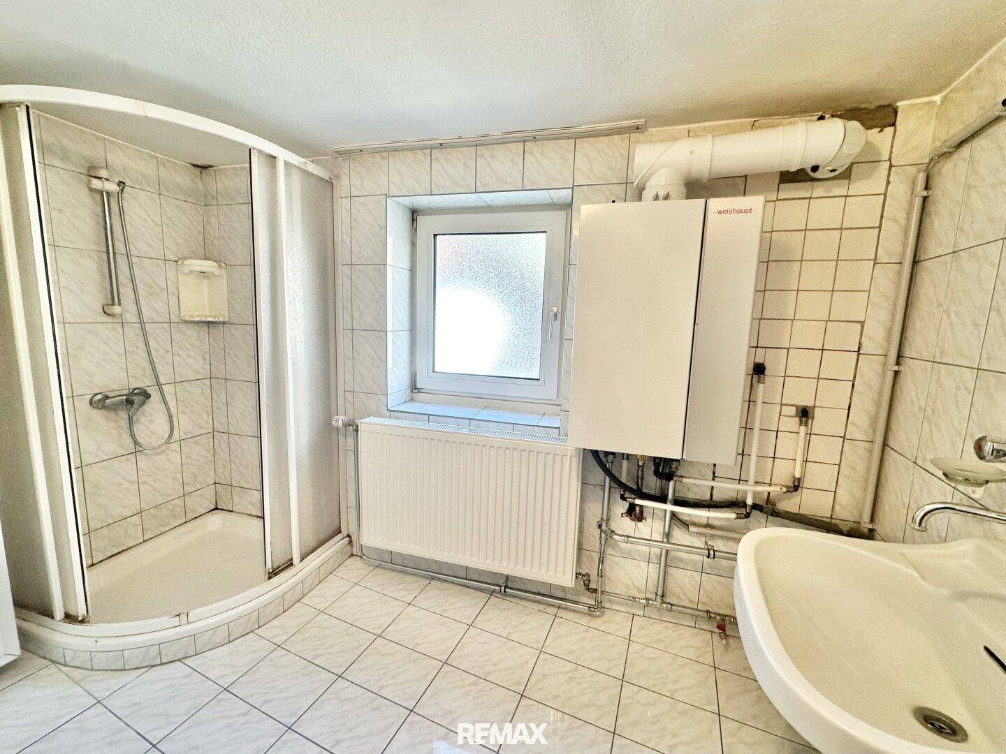 Detaillierte Ansicht des Badezimmers mit Duschkabine, Waschbecken und Heizung.