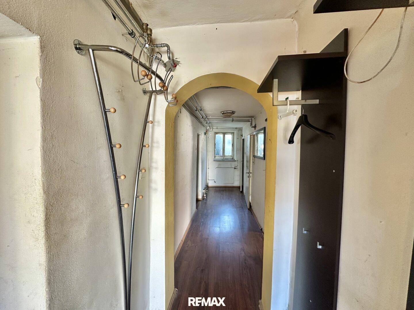Langer Flur mit Holzboden, Garderobe und einem Bogen zum hinteren Bereich.
