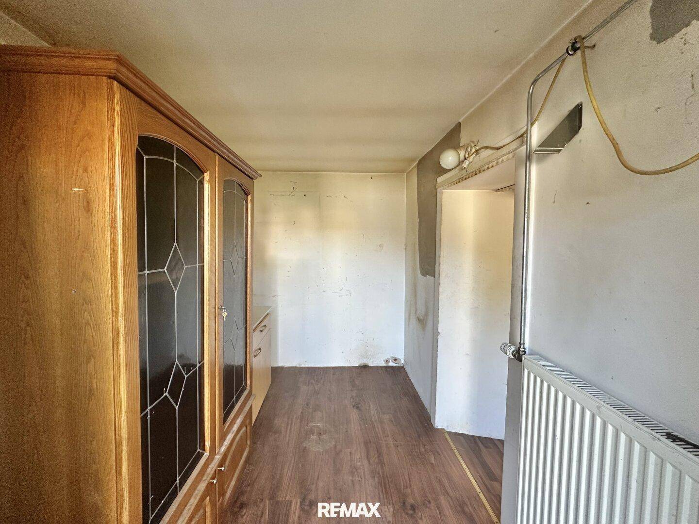 Schmaler Raum mit Holzboden, großem Holzschrank und Heizkörper.