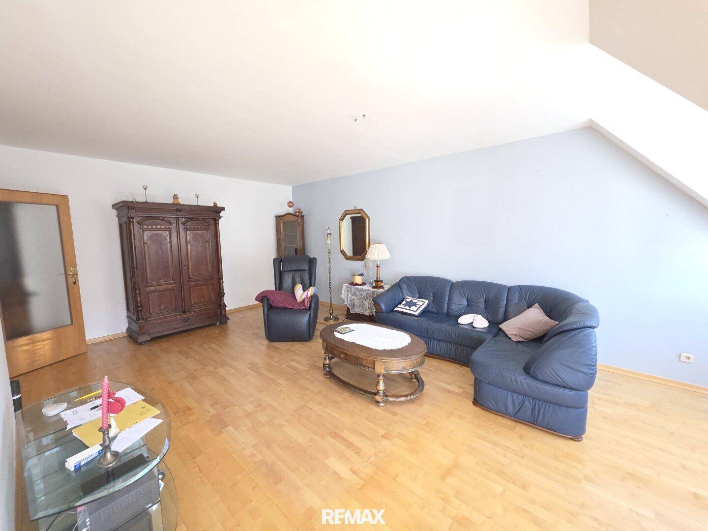 Gemütliches Wohnzimmer mit Holzboden, blauer Couch und traditionellen Holzmöbeln unter Dachschrägen.