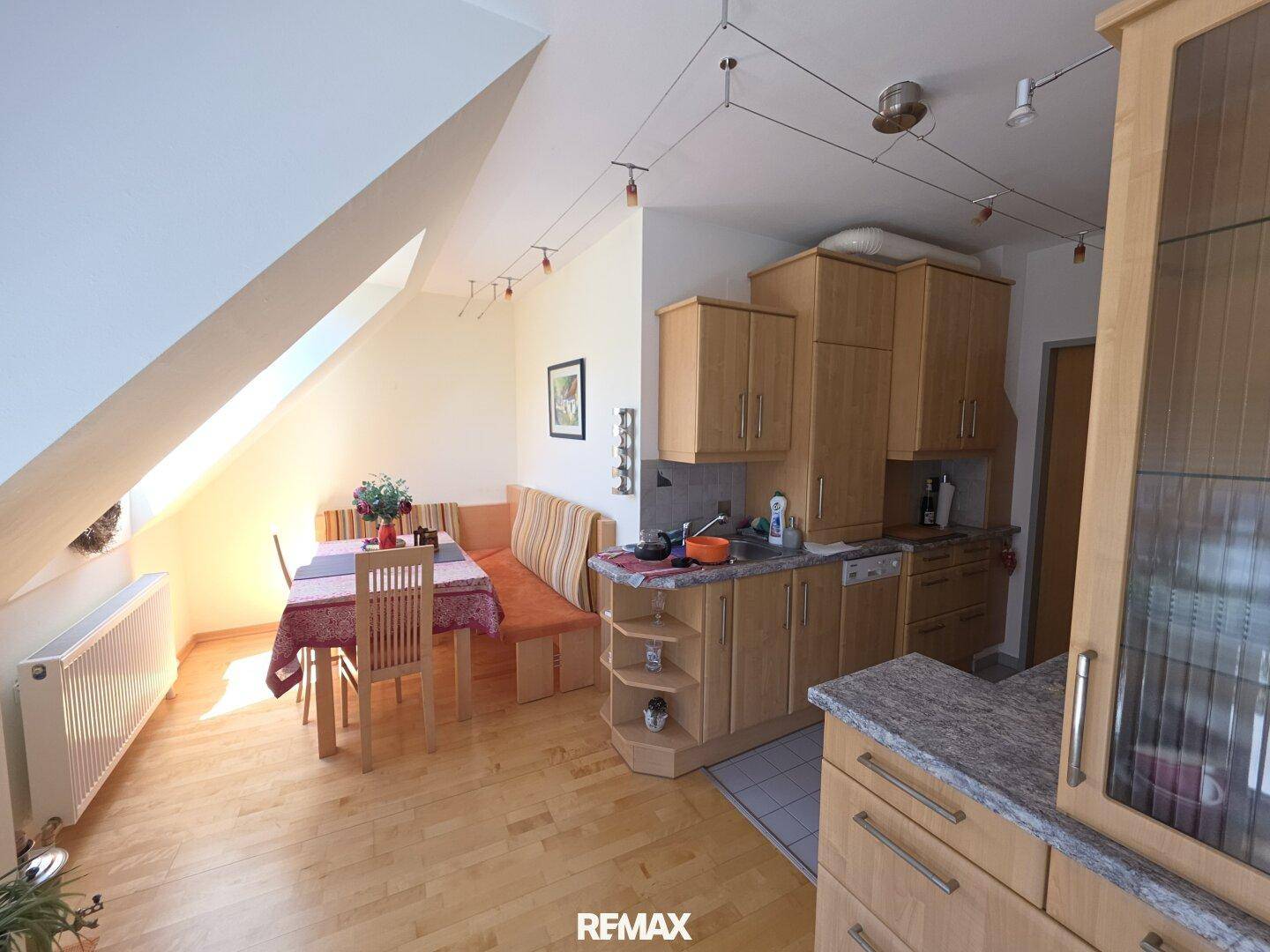 Heller Wohn-Essbereich mit integrierter Küche, Holzboden und Dachschrägen, gut beleuchtet.