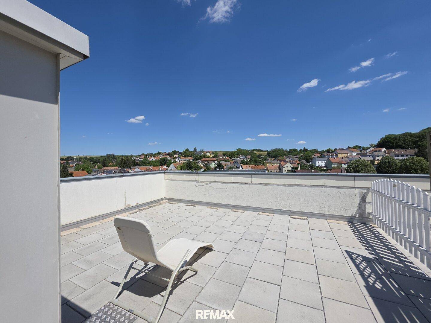 Geräumige Dachterrasse mit hellen Fliesen und Liegestuhl, bietet weiten Blick über die Umgebung.