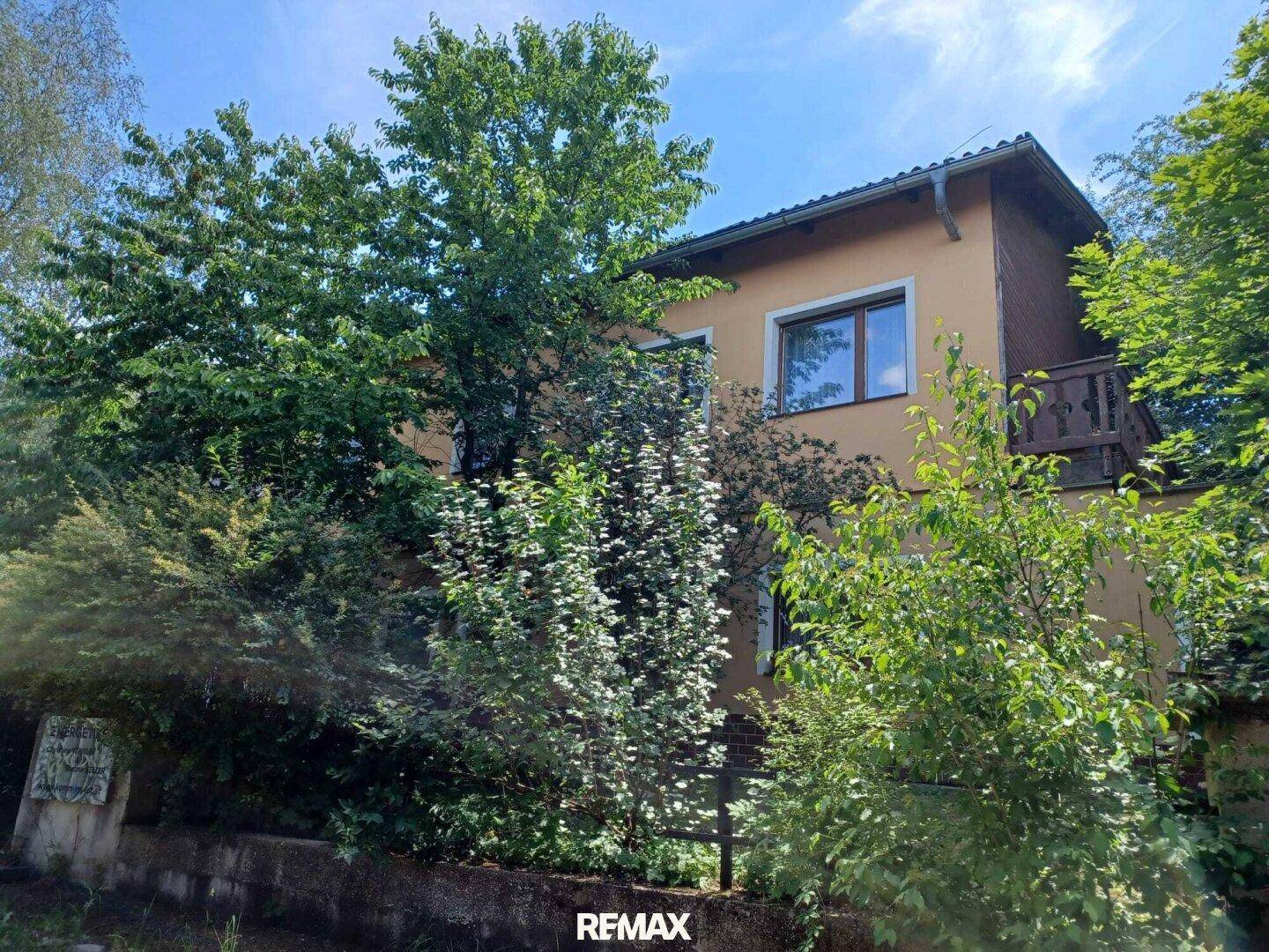 Seitenansicht des Hauses mit Balkon und dichter Vegetation im Vordergrund.