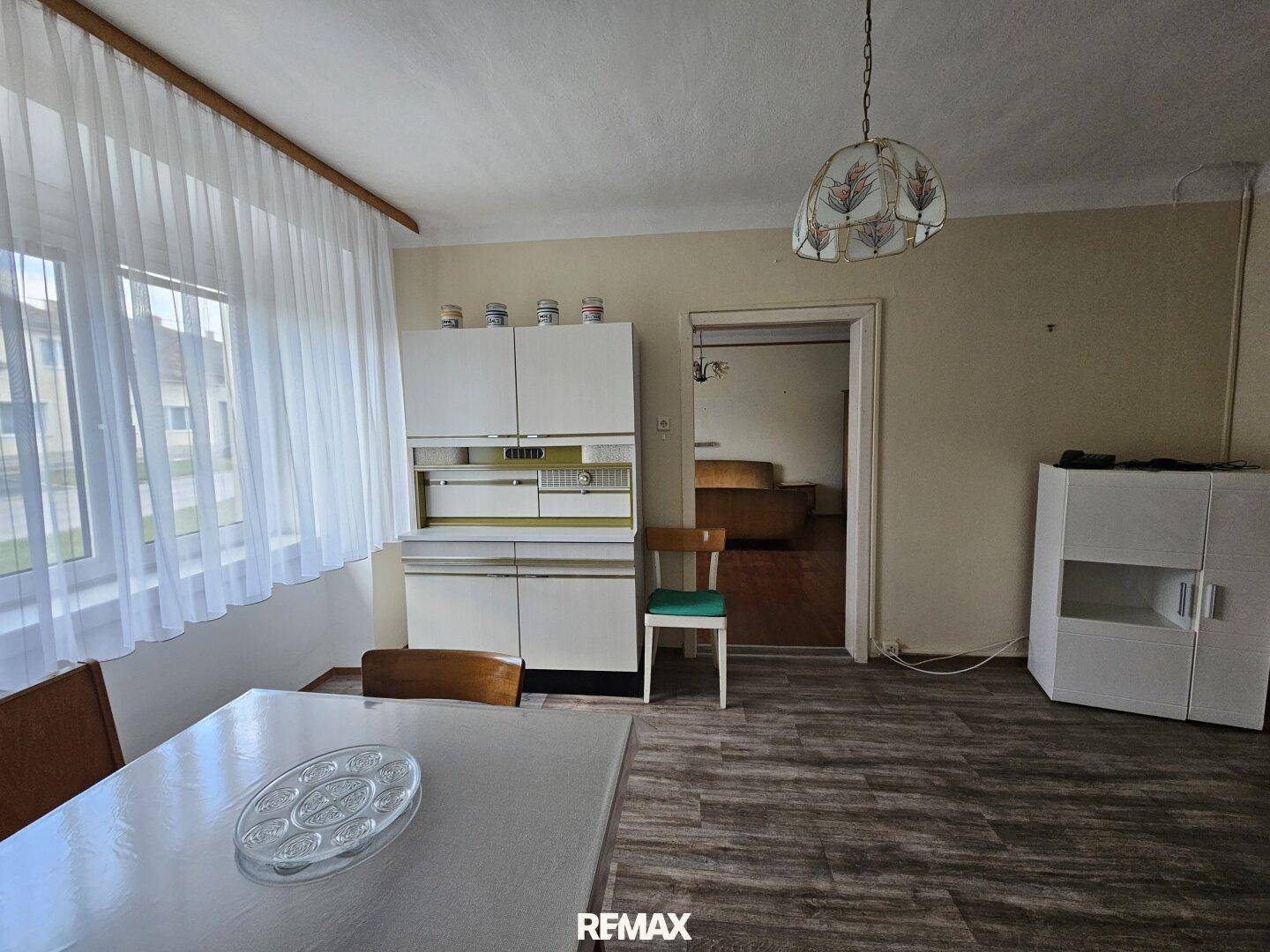 Essbereich in einer älteren Küche mit großem Fenster und Vintage-Möbeln.