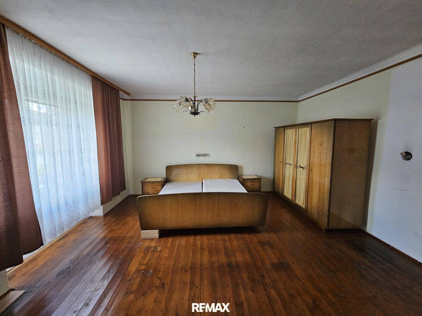 Schlafzimmer mit Holzboden, großem Fenster und Vintage-Doppelbett.