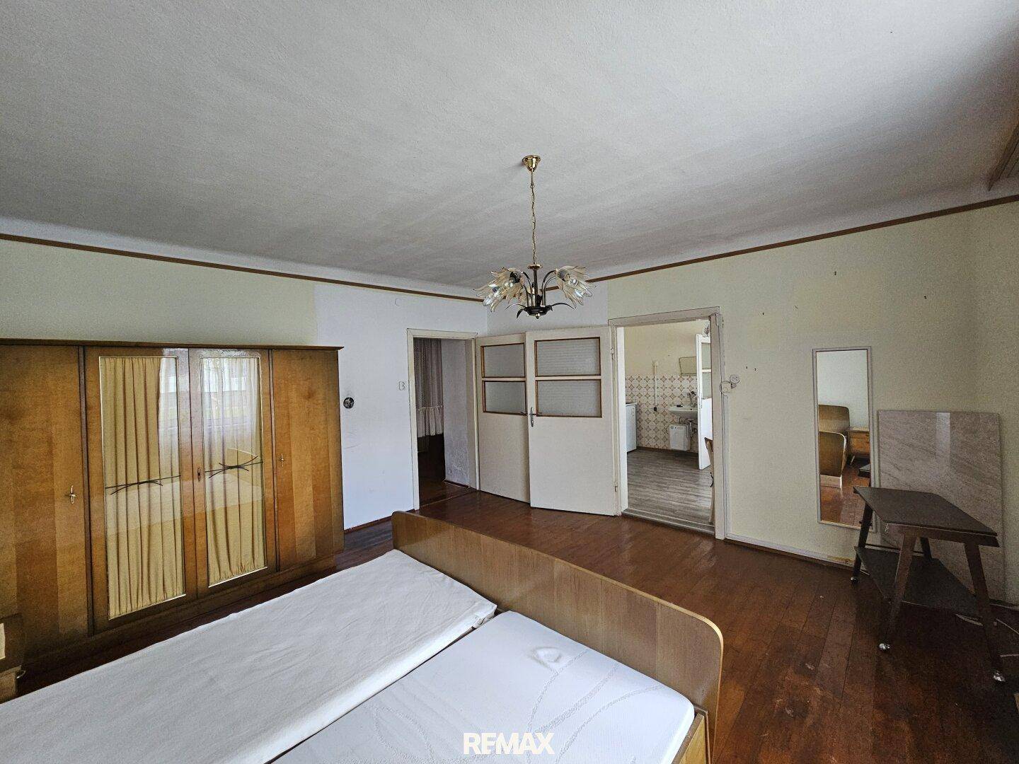 Schlafzimmer mit Holzboden und Blick durch die Tür in einen weiteren Raum.