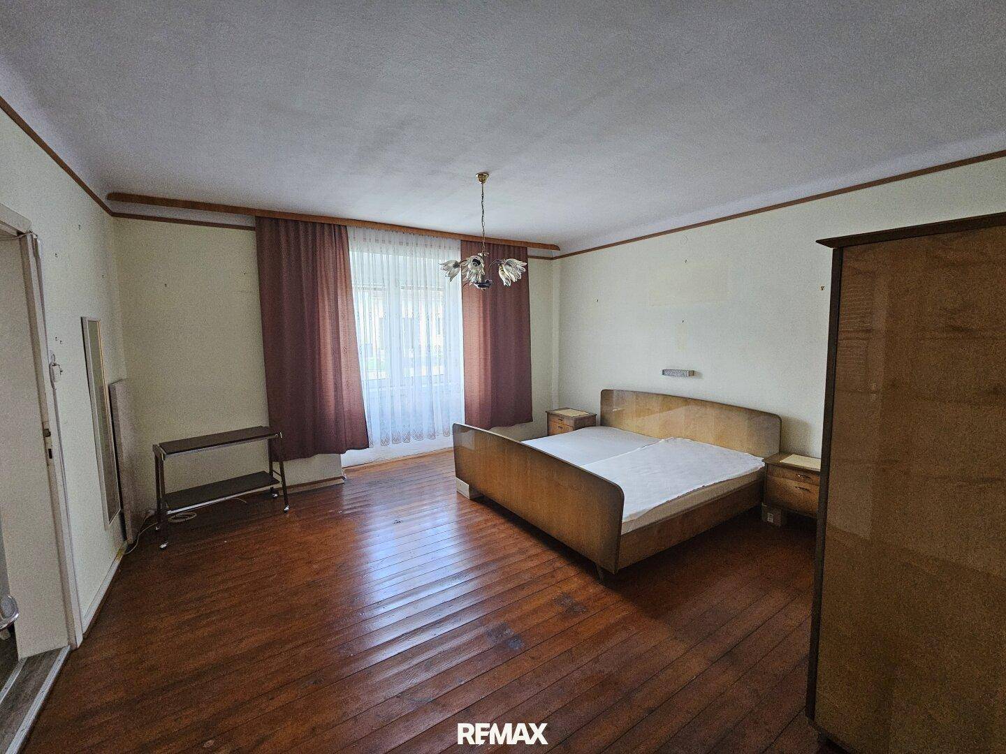 Geräumiges Schlafzimmer mit Holzboden, großem Fenster und Vintage-Möbeln.